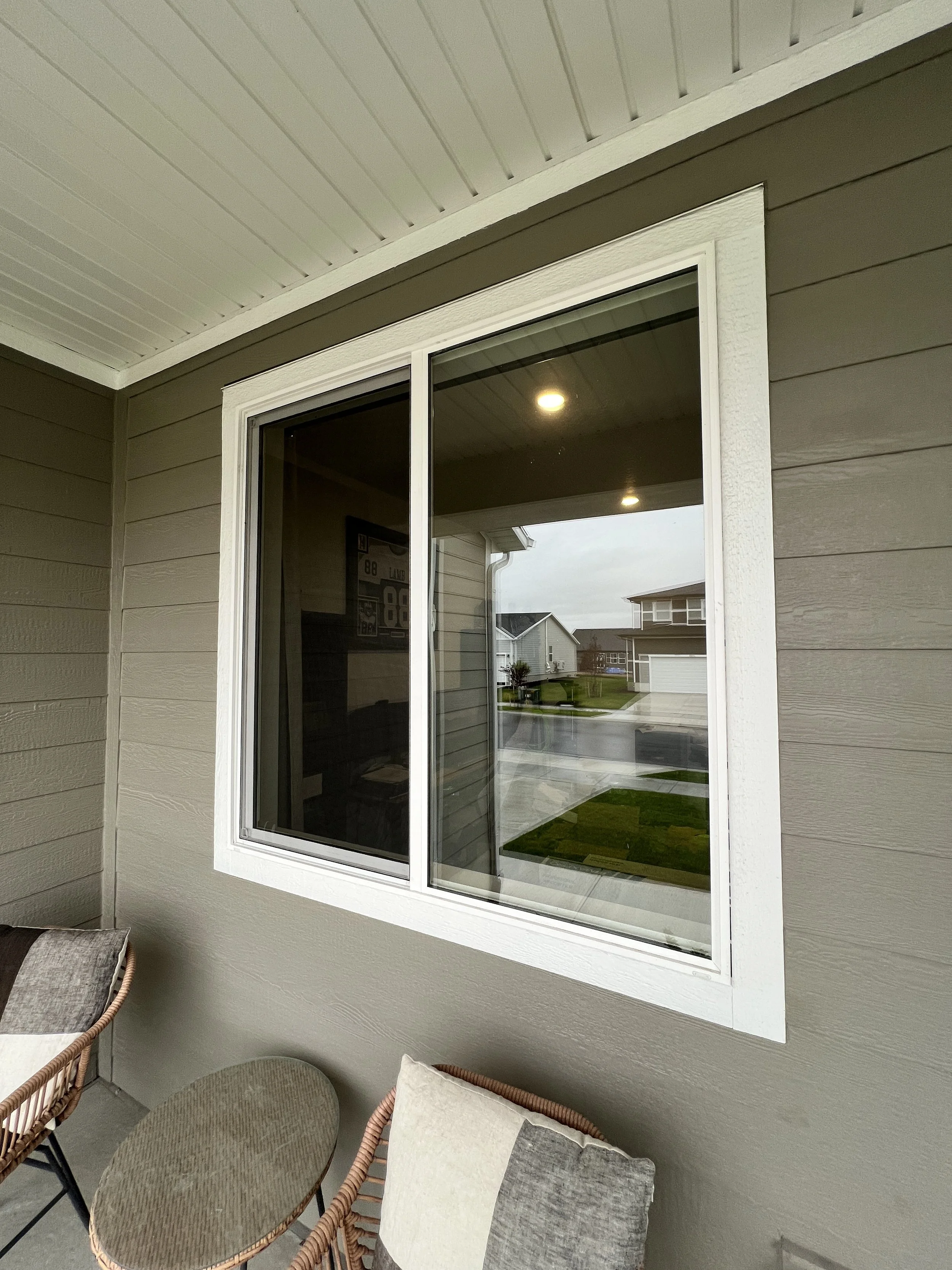 Residential porch with a gray wall, a large window, and outdoor seating including wicker chairs with cushions.