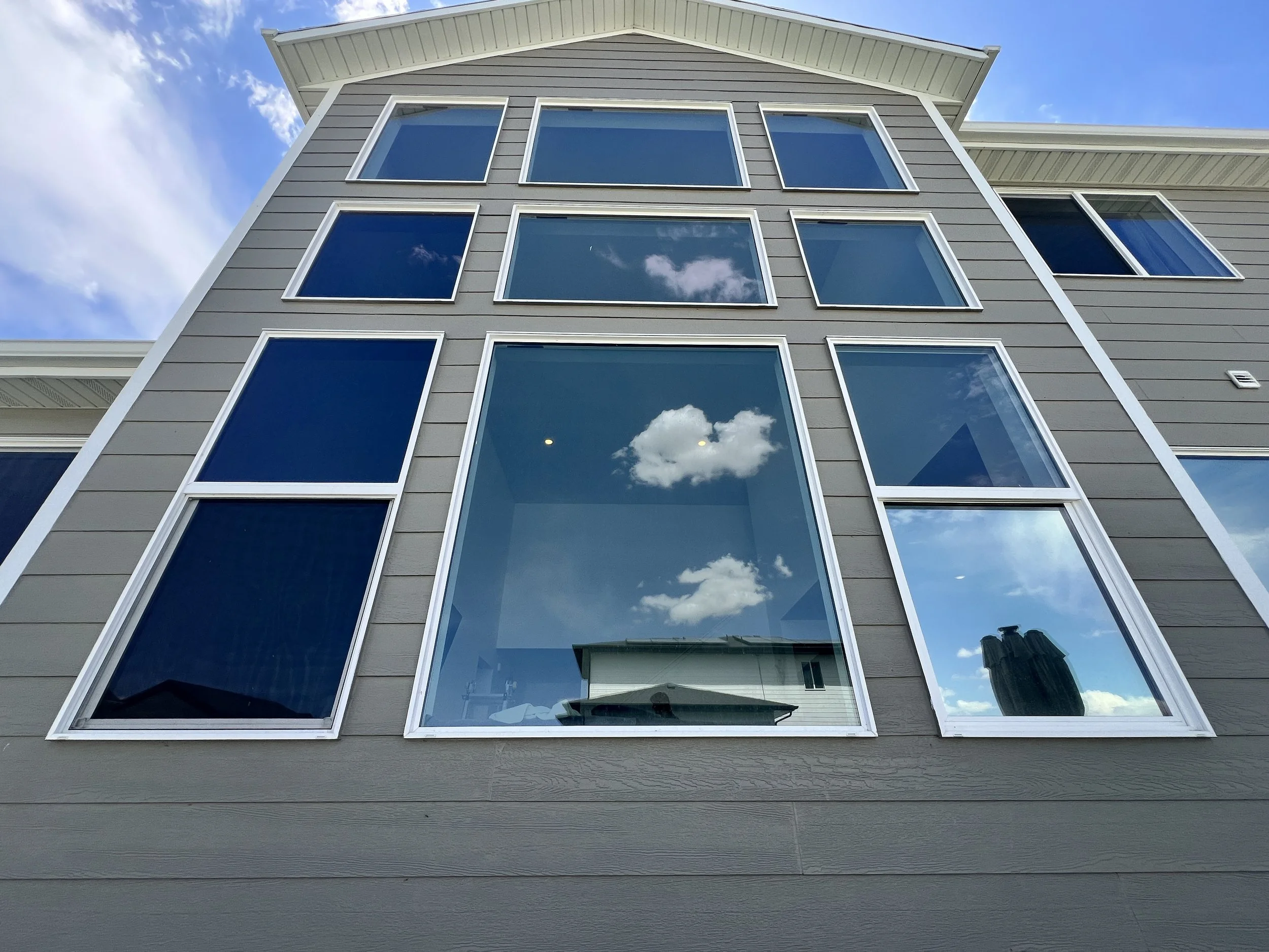 Exterior view of a modern house with large, multi-pane windows reflecting the blue sky and clouds.