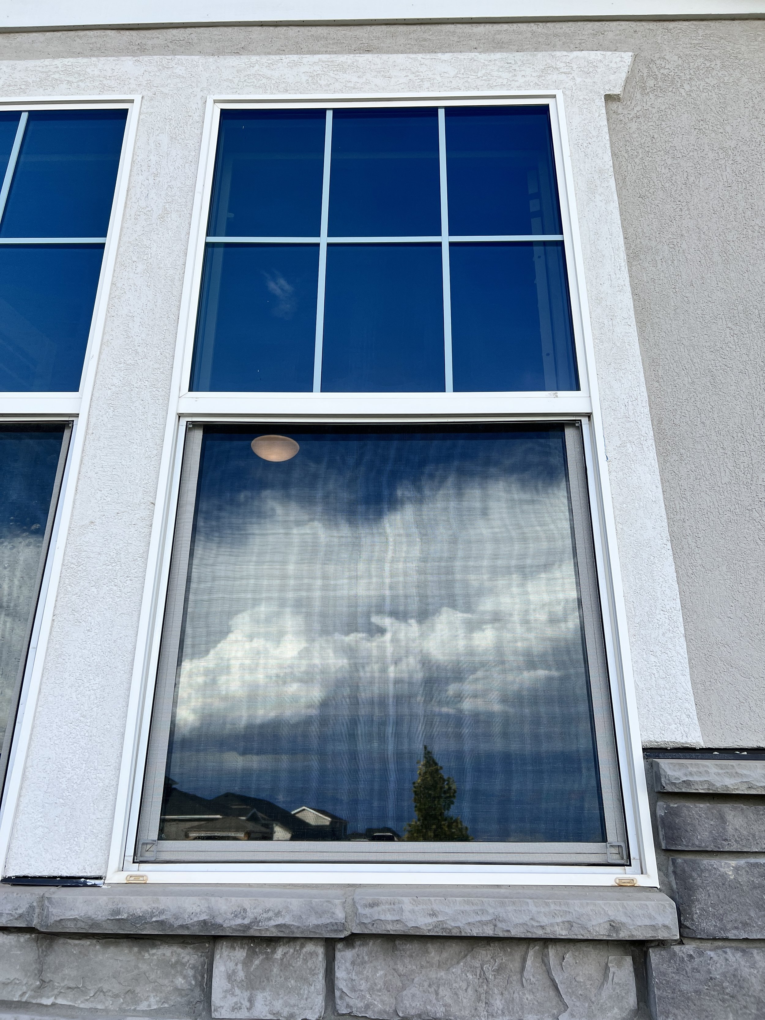 Close-up of a window reflecting a cloudy sky and partly visible houses and trees.