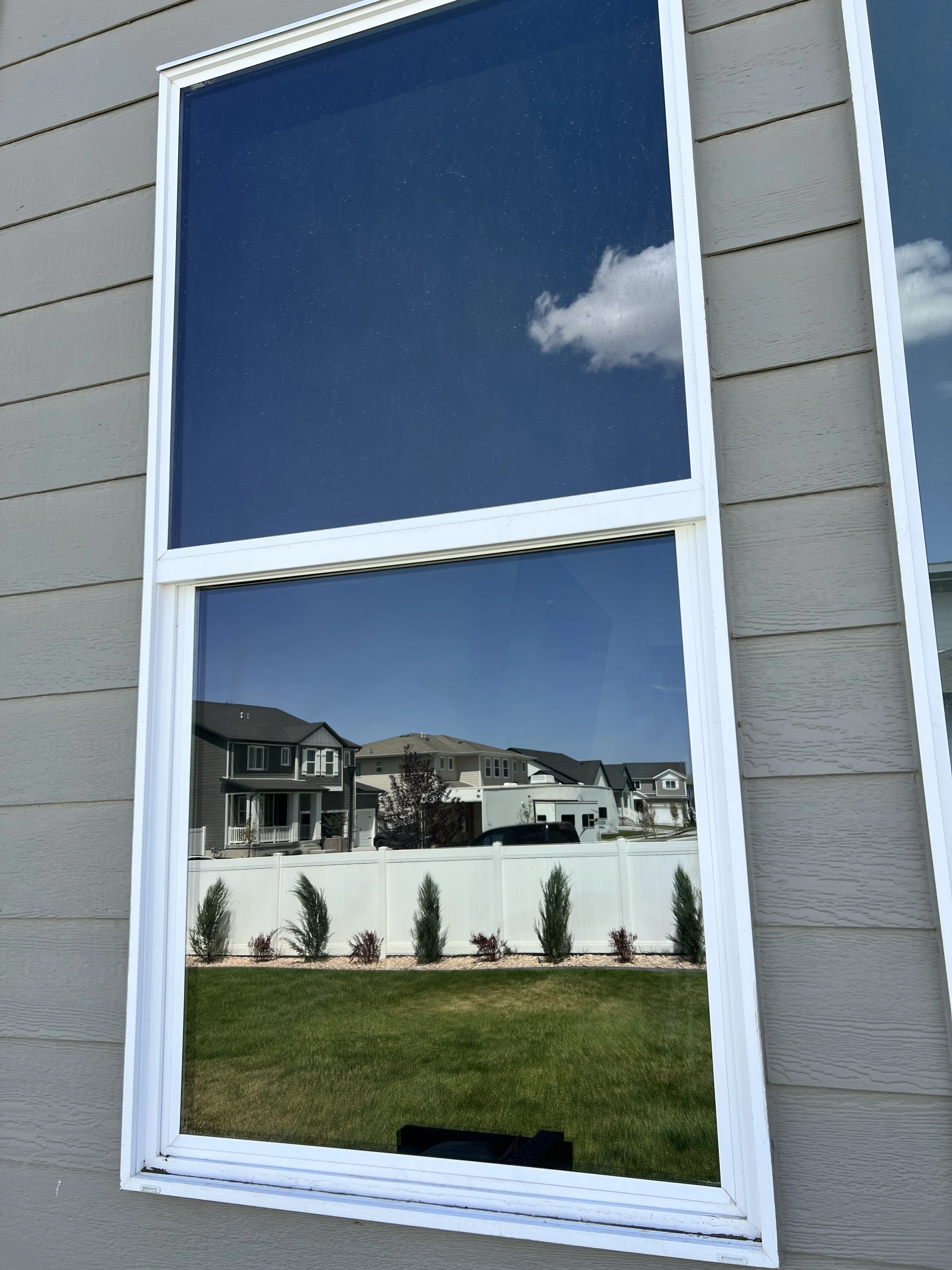 Reflection of neighboring houses and sky with clouds in the window of a beige house.