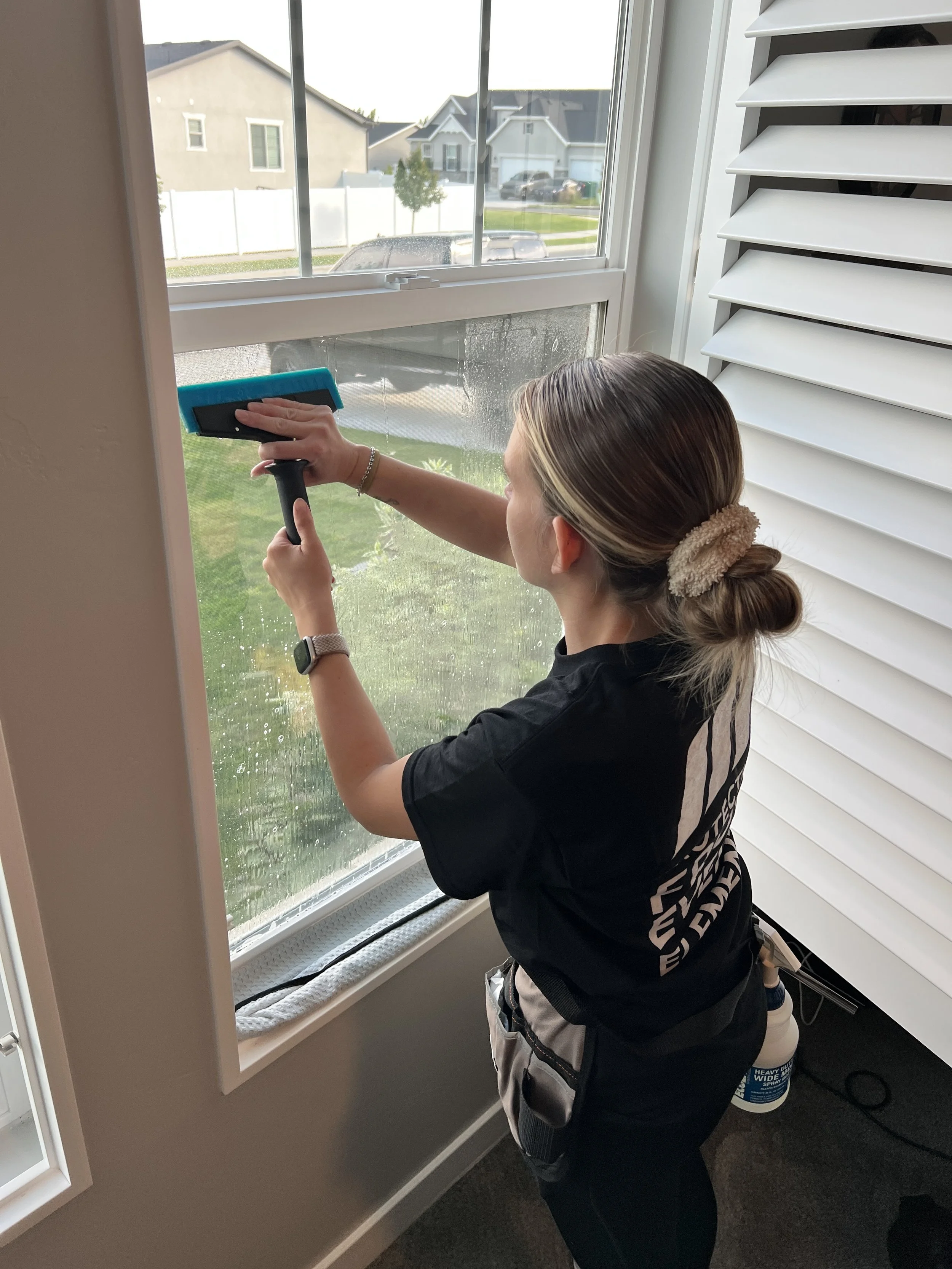 A woman cleaning a large window with a squeegee inside a house.