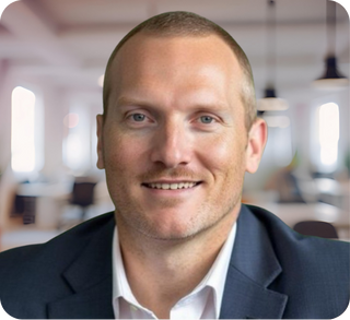 Close-up of a smiling man in a navy blue suit and white shirt, in an office setting with blurred background.