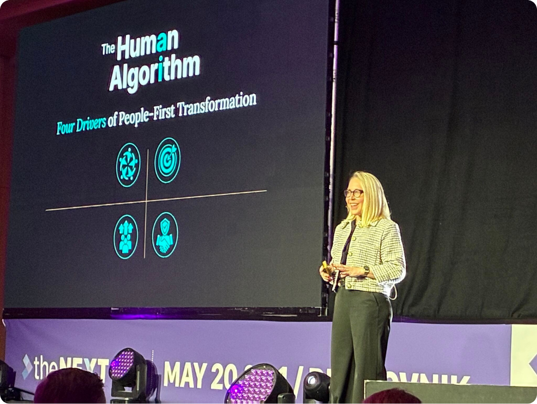 Presenter delivers “The Human Algorithm” presentation; slide shows four icons representing people‑first transformation drivers.
