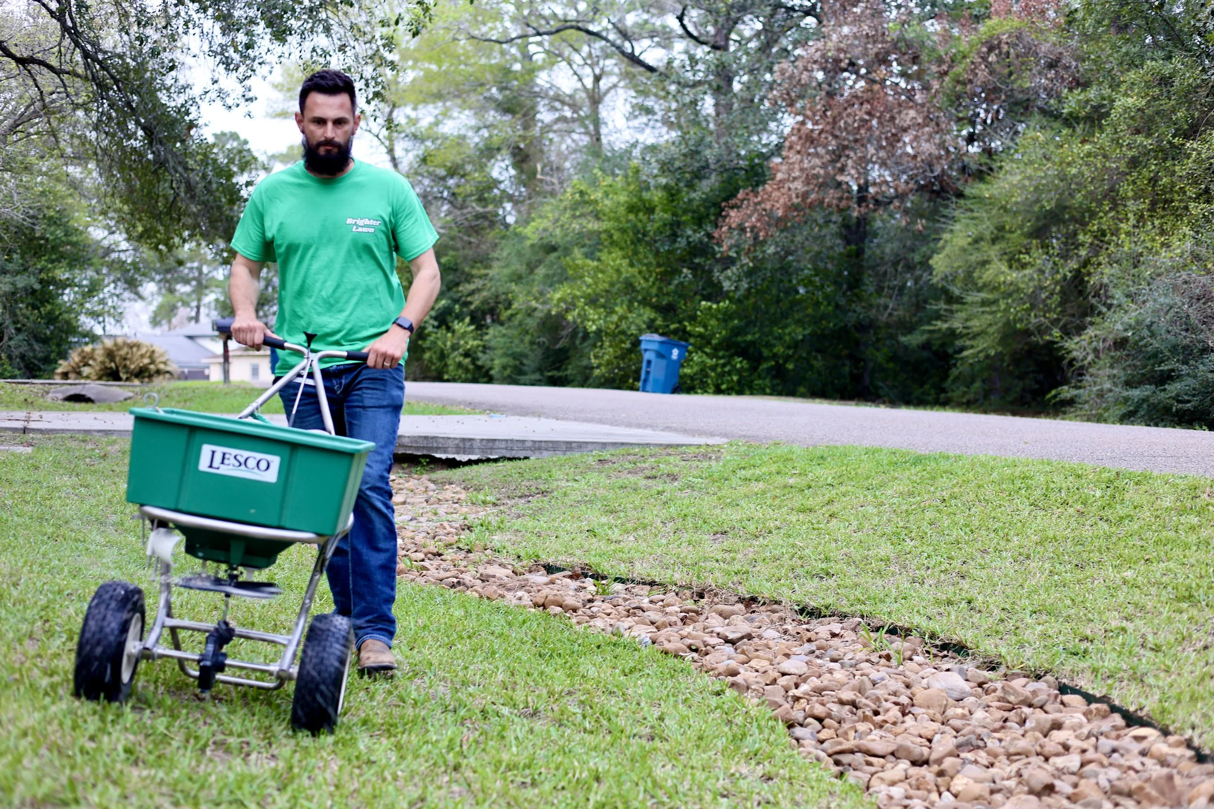 A Brighter Lawn team member pushing a Lesco spreader spreading fertilizer in a customers lawn.