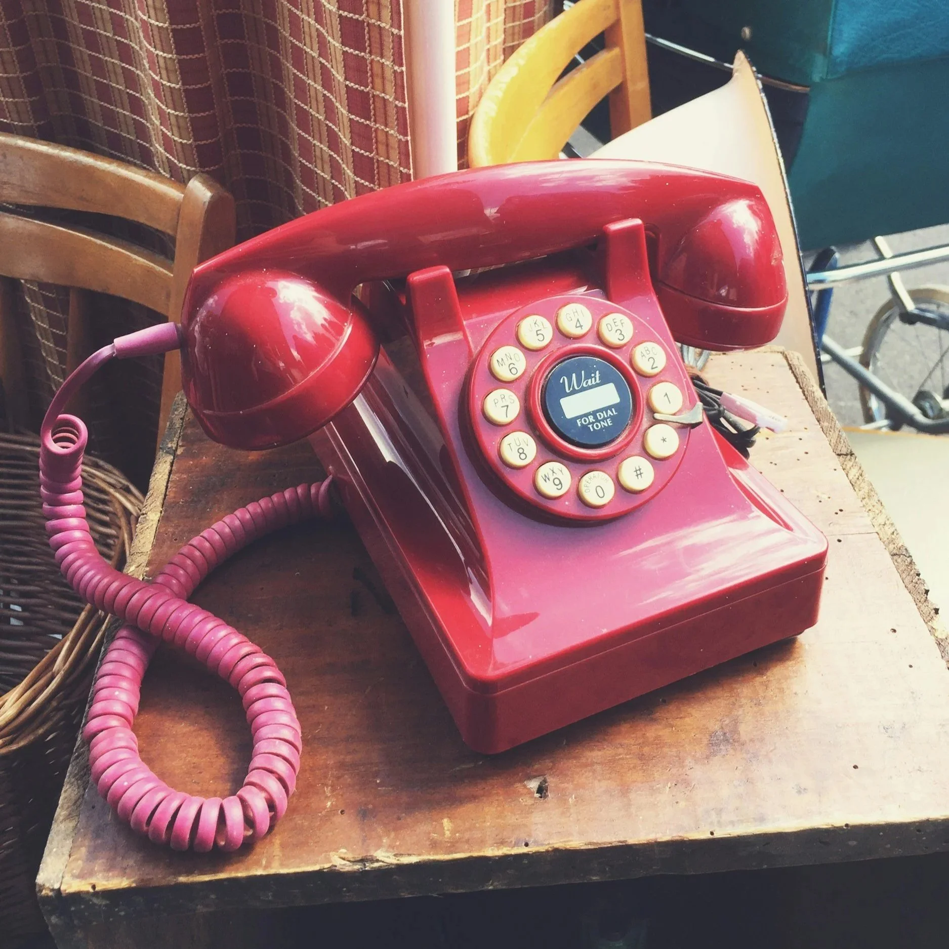 A vintage red rotary dial telephone sitting on a wooden table with a pendulum cord and a digit display in the center.