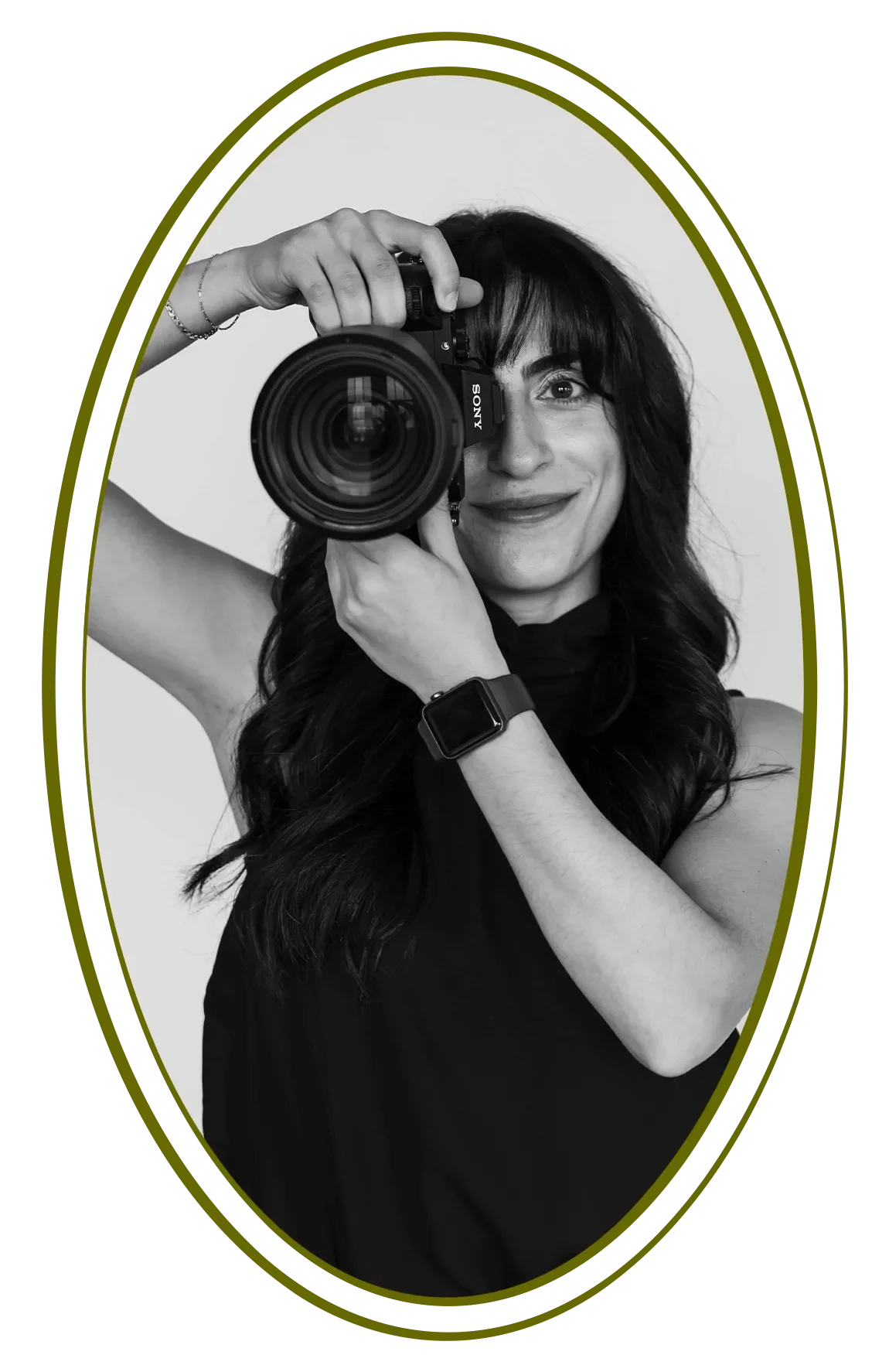 Black and white photo of a woman taking a selfie with a camera, smiling, wearing a sleeveless top, and a smartwatch on her wrist, framed within an oval border.