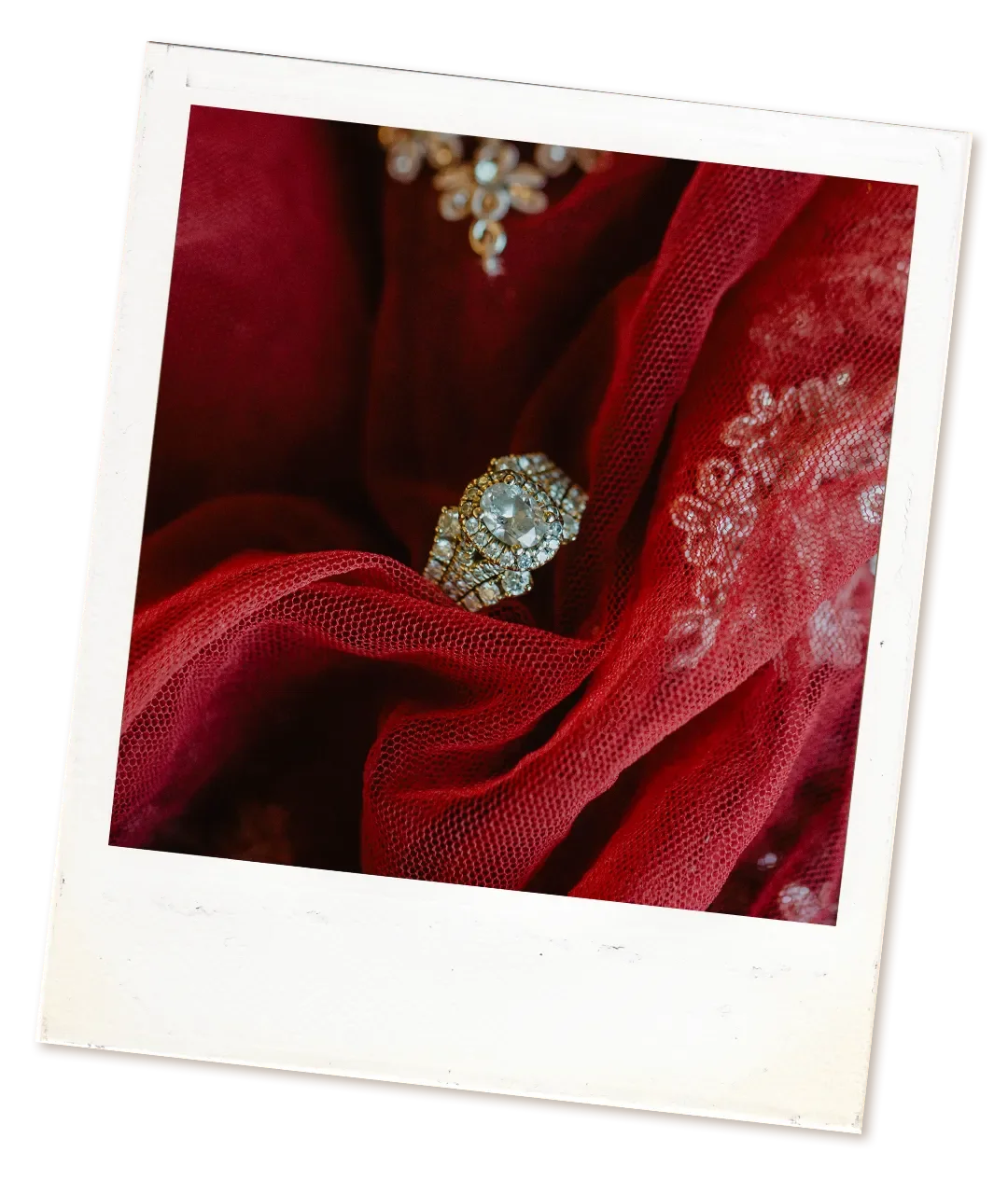 A close-up of a diamond ring with a large central stone surrounded by smaller diamonds, resting on soft red lace fabric, traditional in Indian weddings.