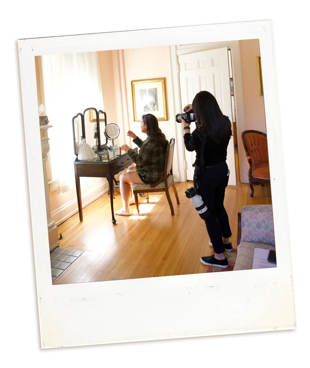 Bride sitting at a vanity table getting ready, while a photographer with a camera takes pictures in a cozy, well-lit room.