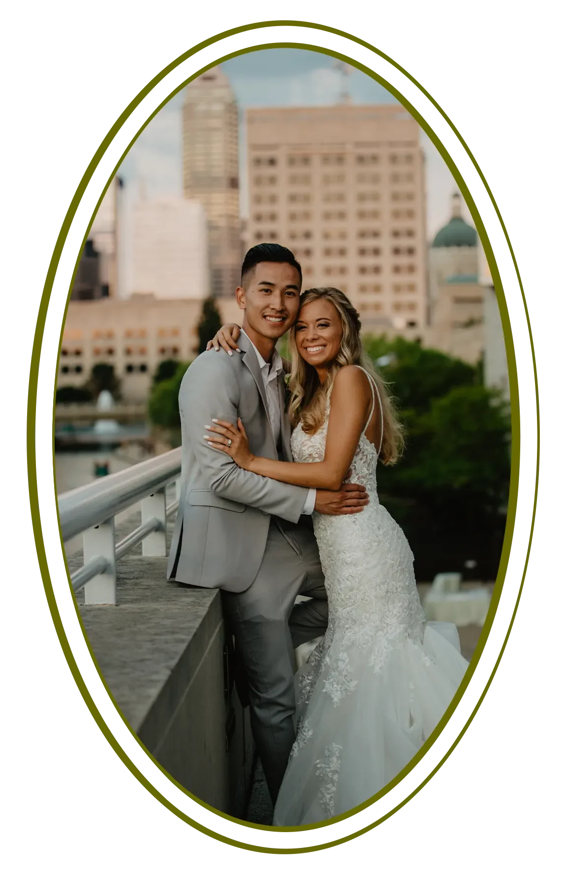 A happy couple in wedding attire embracing outdoors with city skyline in the background.