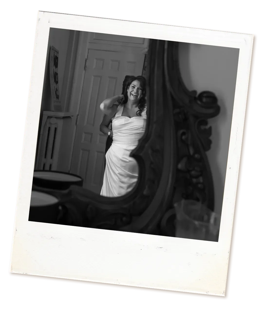 A woman in a strapless wedding dress is looking into a mirror and smiling.