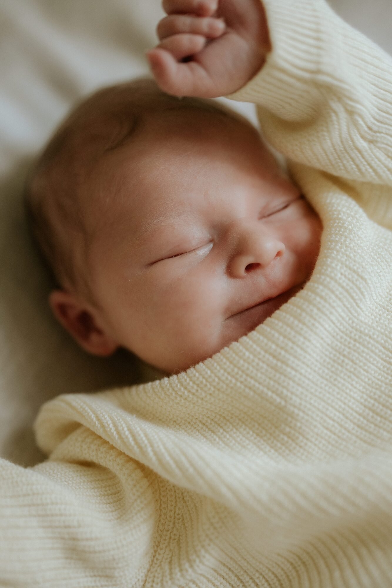 Beeld van een slapende baby, ingepakt in een lichtgele trui.