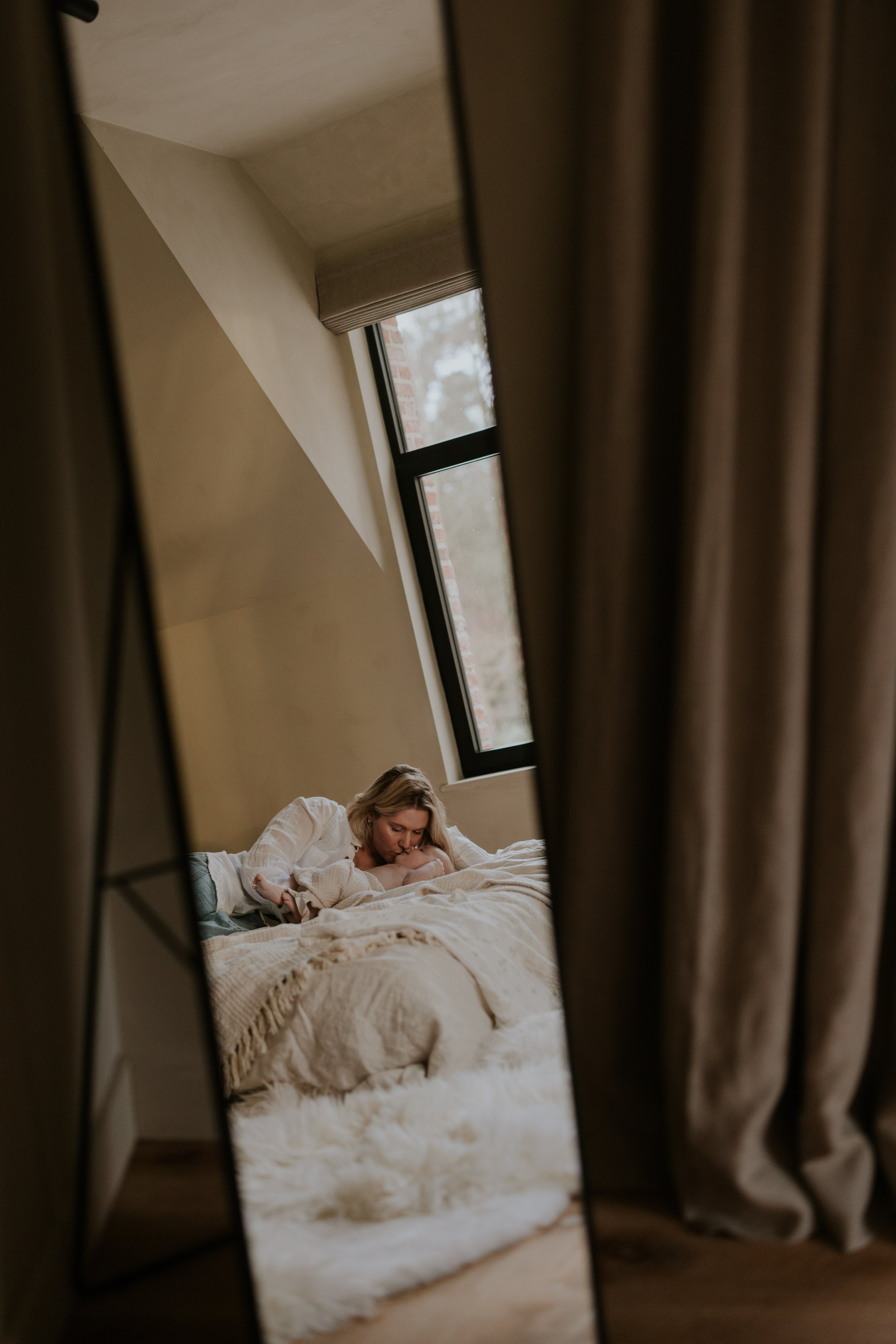 Een vrouw die in bed ligt, gezien via een spiegel, met een raam op de achtergrond.