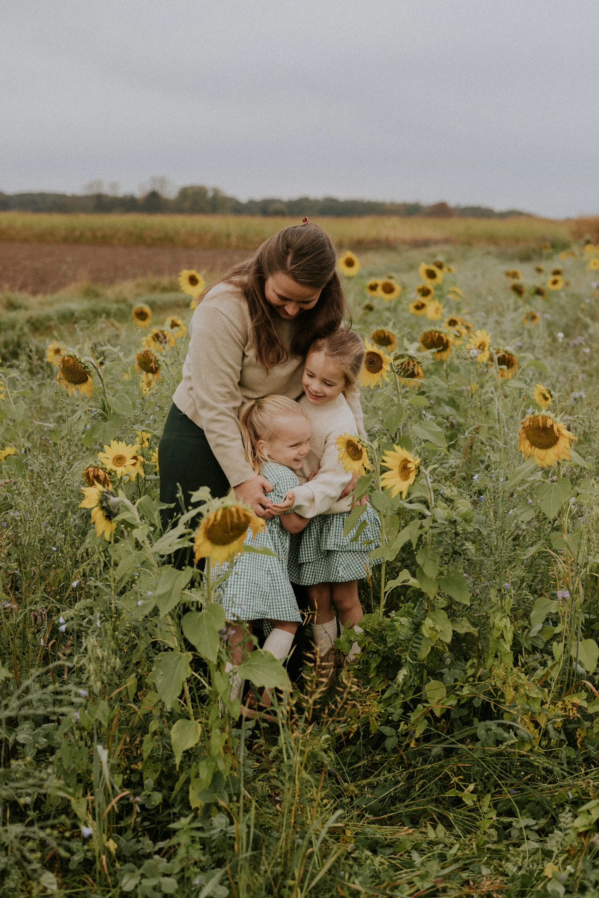 Vrouw en drie jonge meisjes omhelzen elkaar in een veld met zonnebloemen.