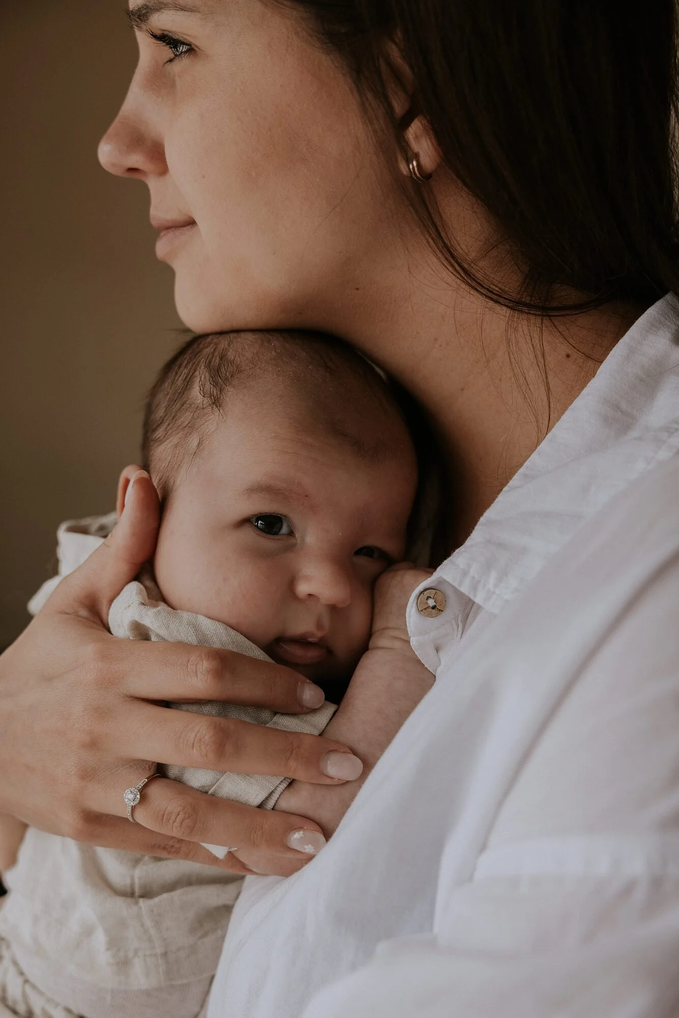 Close-up van een vrouw die haar jonge baby vasthoudt, met de baby die in haar armen knuffelt en kijkt naar de camera.