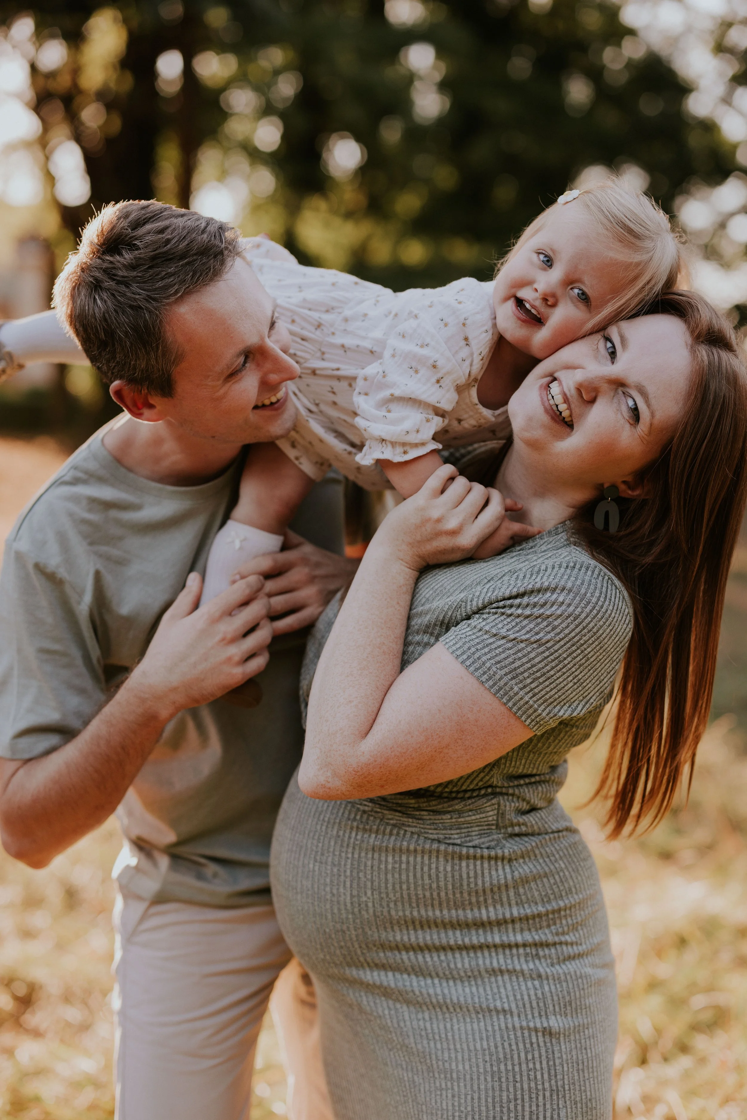 Een lachend gezin met een man, een vrouw en een jong meisje die samen buiten in de natuur spelen.
