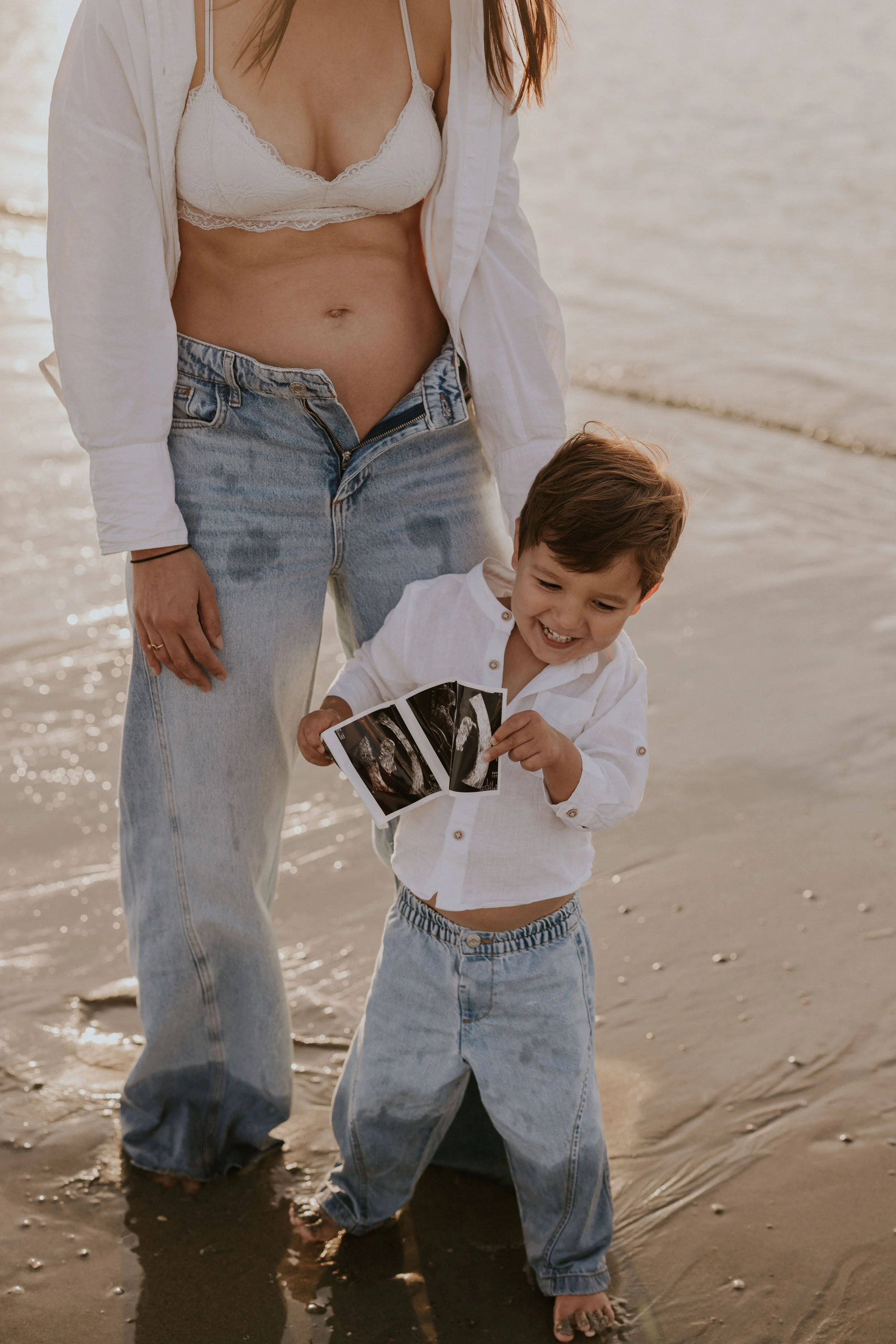 Vrouw en kind op het strand, ze houden een echo van de zwangerschap, omgeven door water en zand.