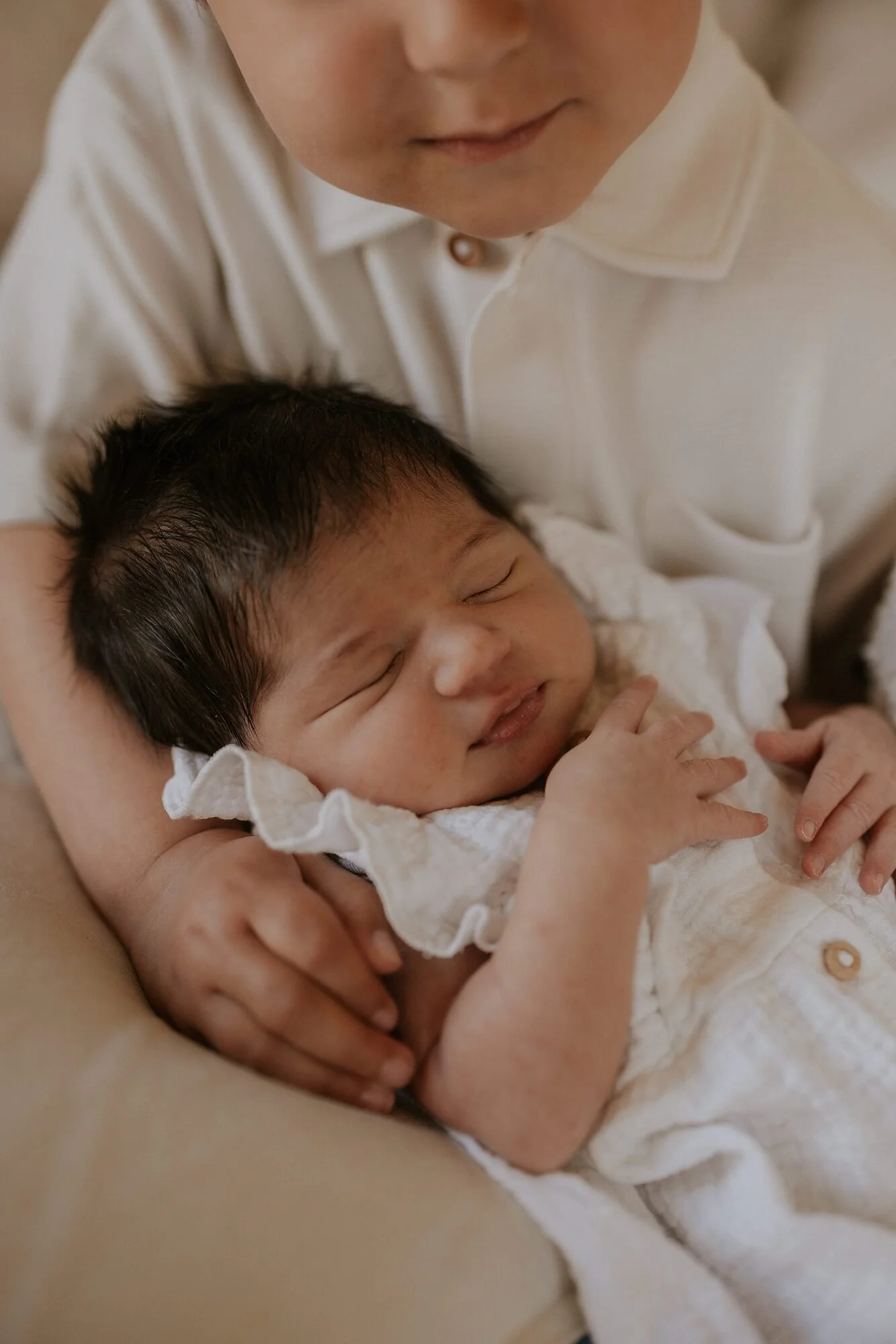 Een close-up van een baby die comfortabel slaapt terwijl ze in de armen van een volwassene ligt, beide dragen witte kleding.