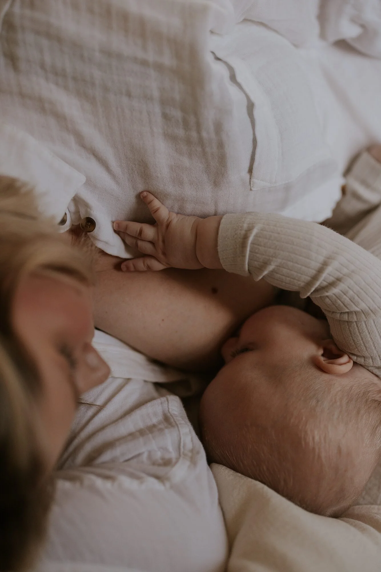 Een vrouw met blond haar en een kind drinken samen borstvoeding, liggend op een bed, in een warme en intieme setting.