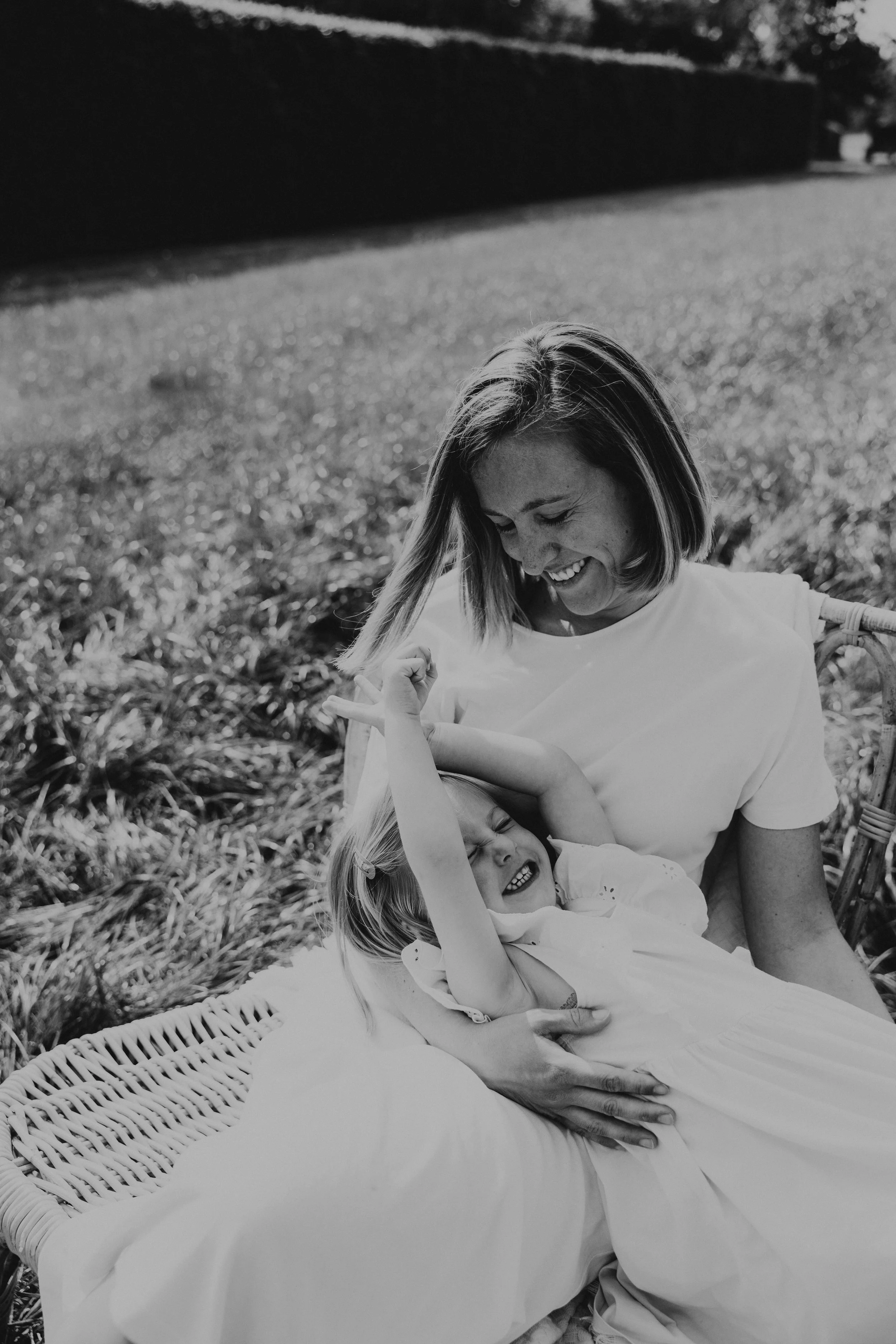 Een vrouw en een jong meisje, lachend en spelend op een grasveld, in zwart-wit.