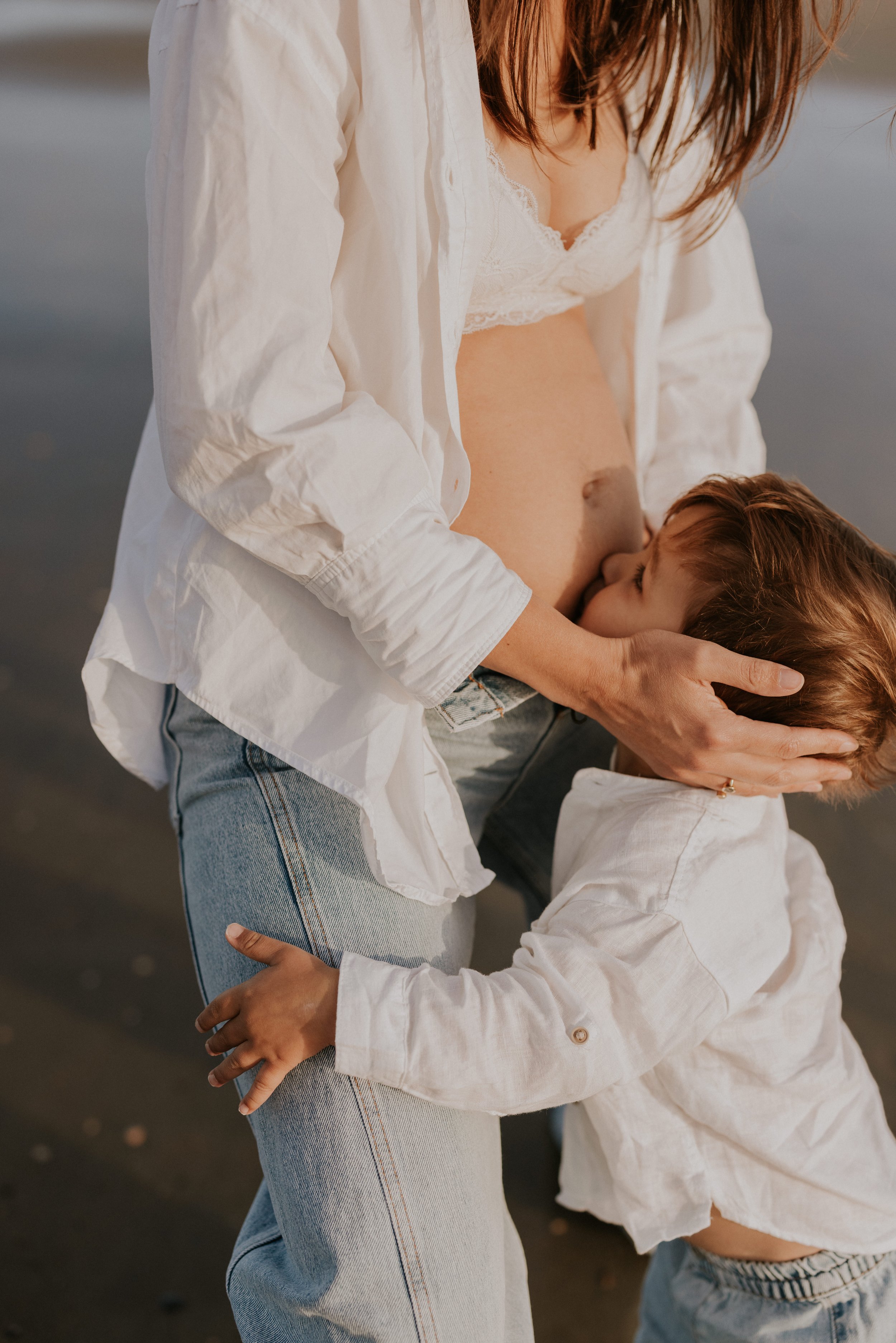 Een zwangere vrouw krijgt een knuffel van haar kleuter, terwijl ze samen aan het genieten zijn op het strand.