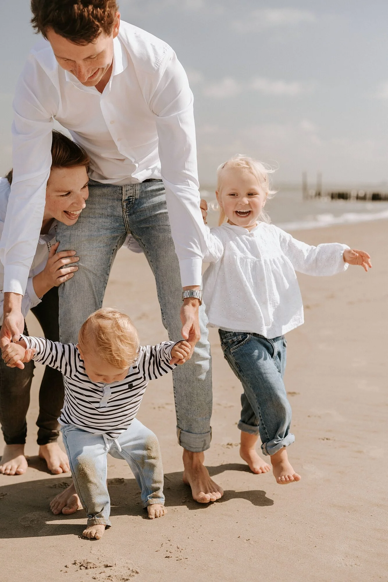 Gezin met kinderen op het strand dat samen een rij gevormd door de zandruimte wandelt.