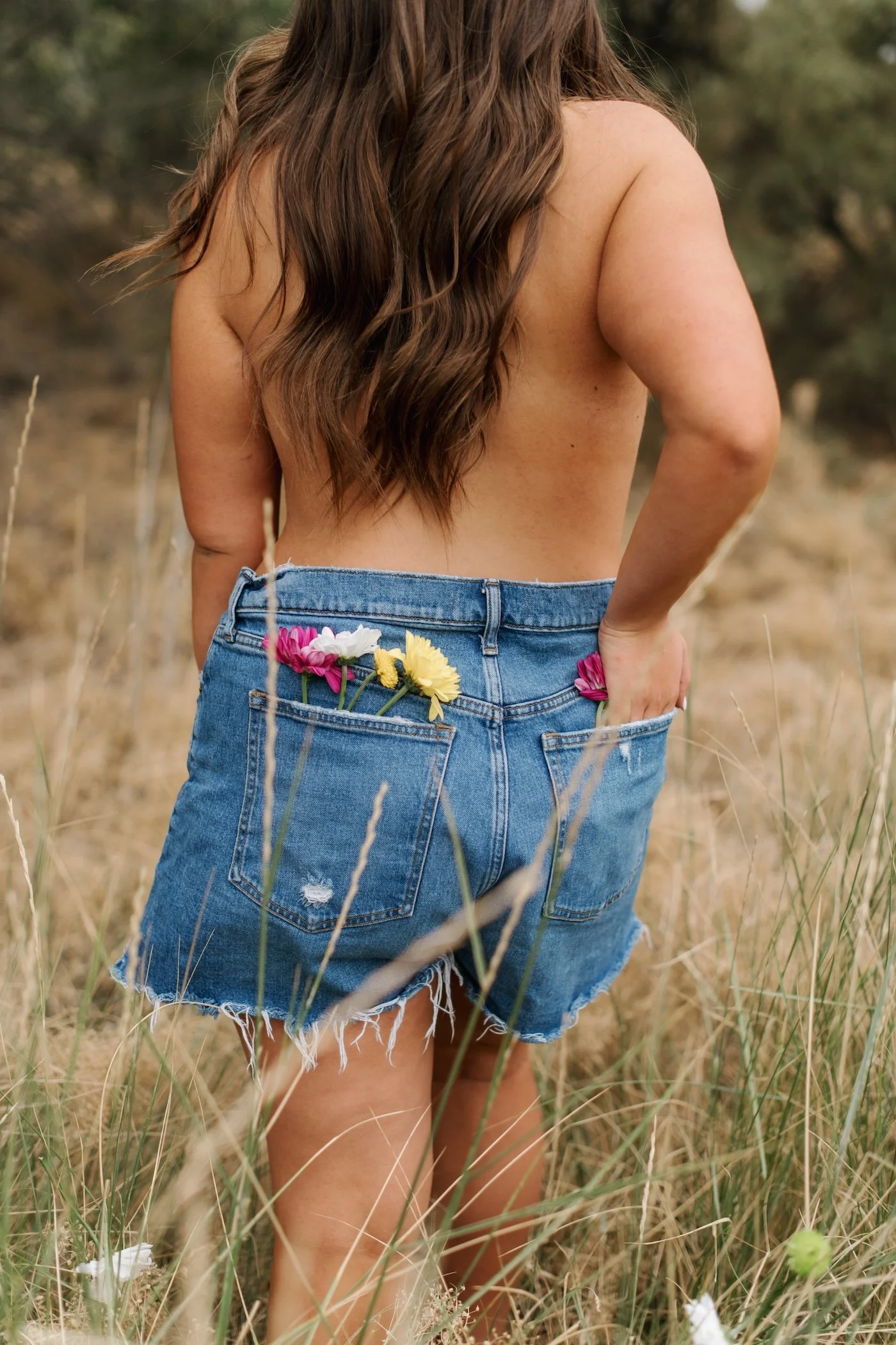 Tanned woman with no shirt on with flowers in her pocket