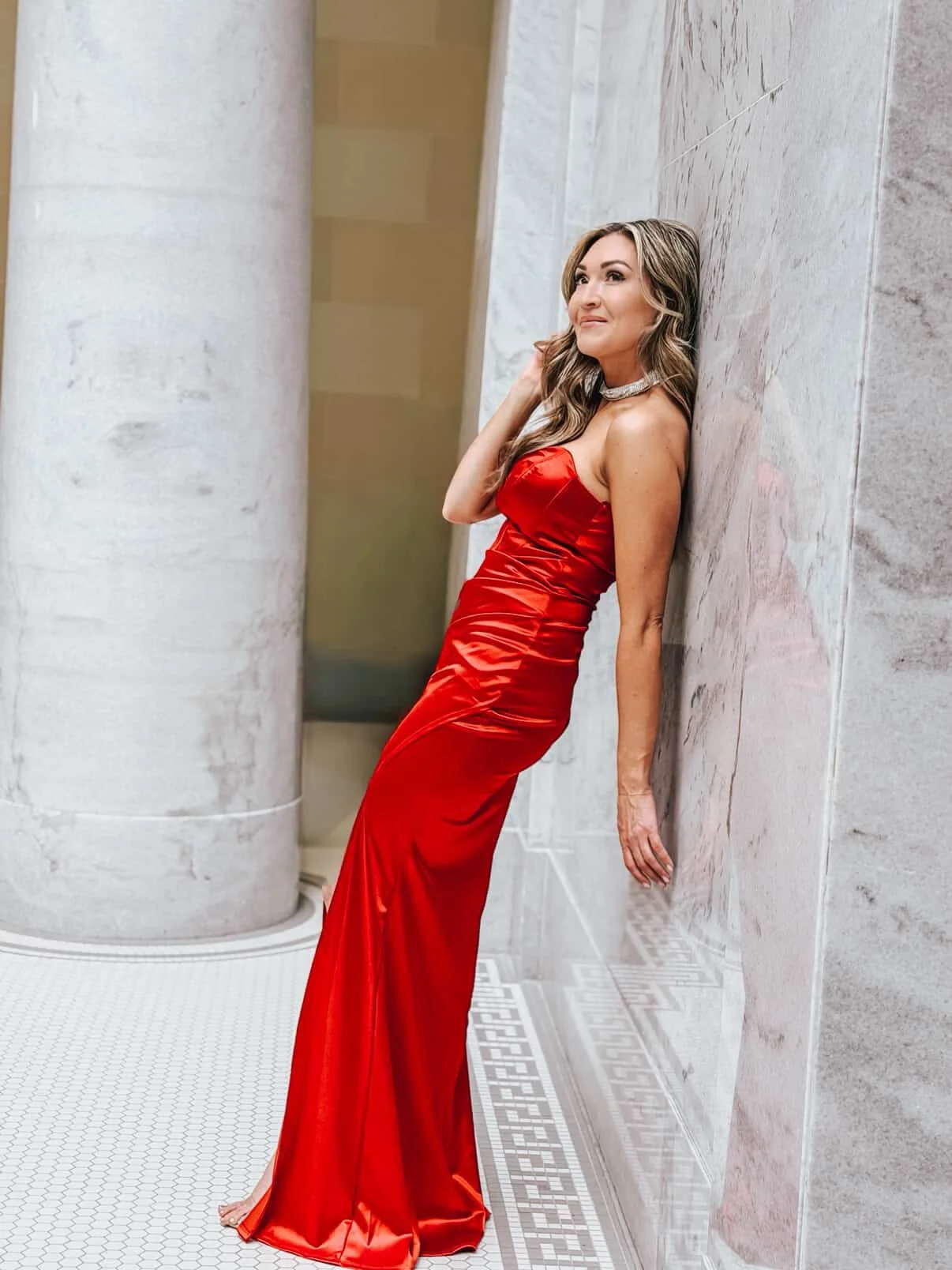 A woman leaning against the wall in a red dress and airbrushed with a fresh color matched spray tan