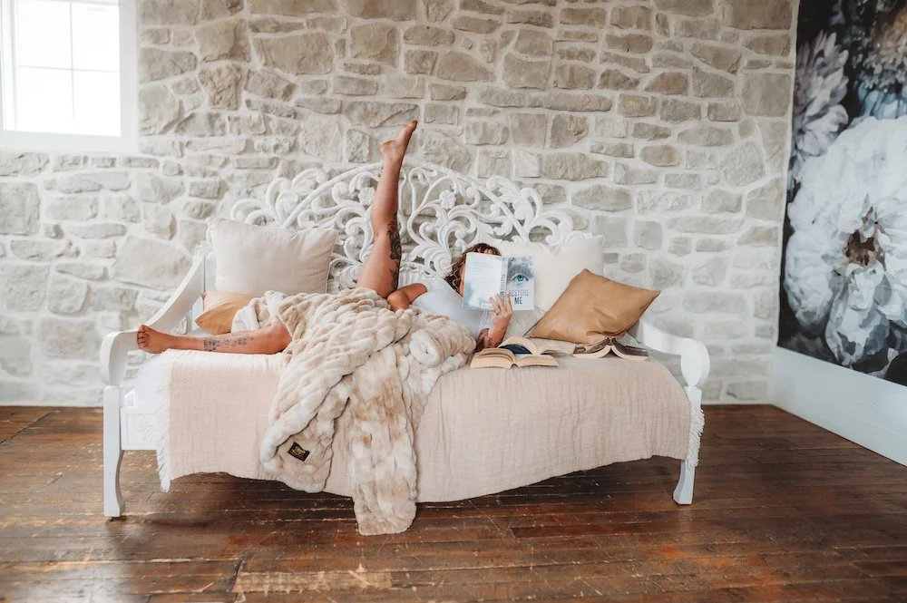 Tanned woman lying in a bed reading a book