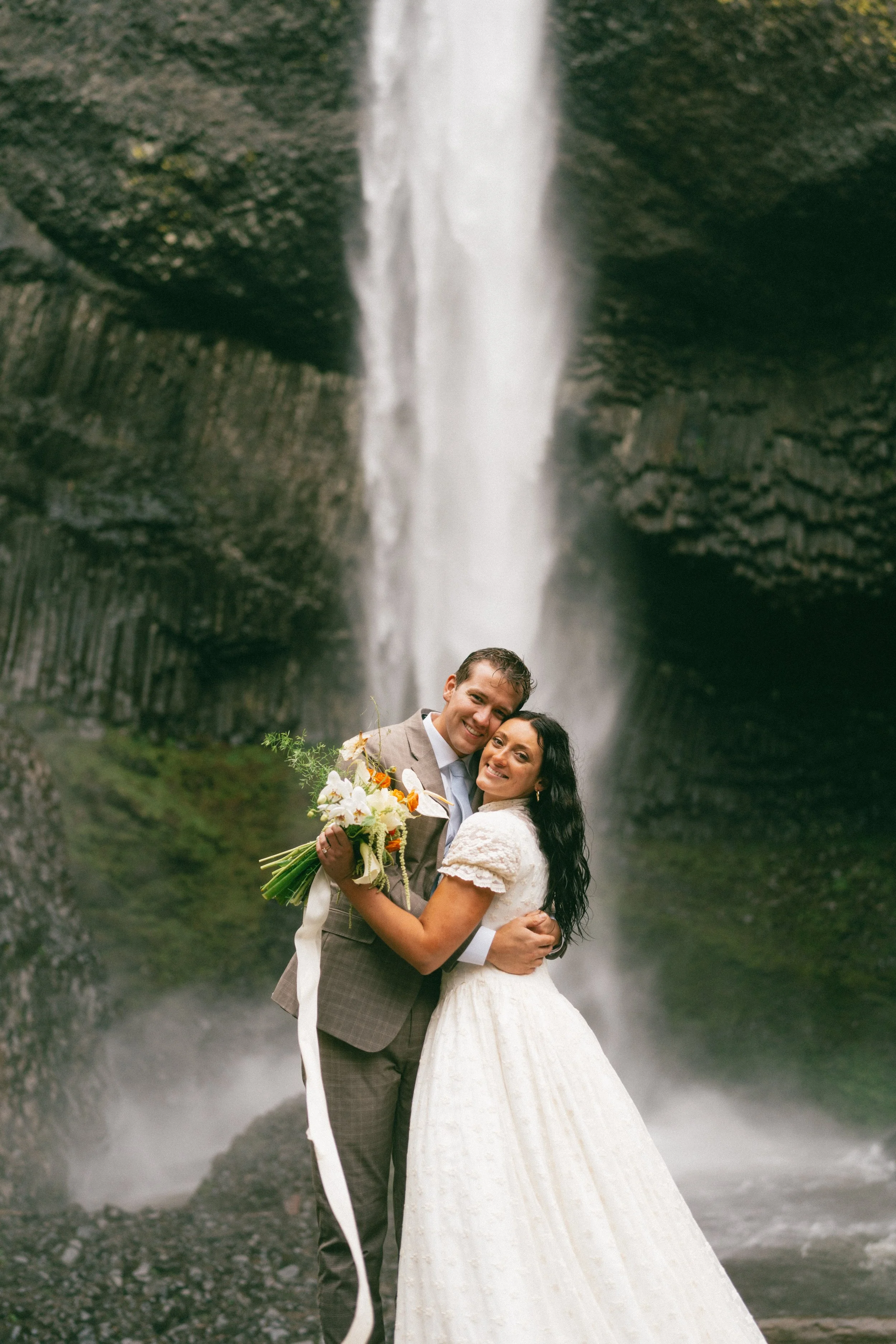airbrushed bride embracing partner in front of waterfall