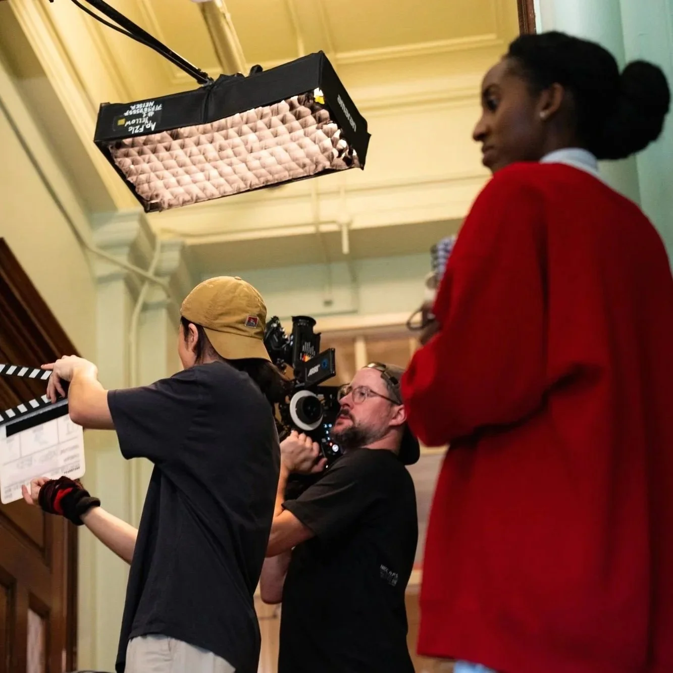 People working on a film set with a camera and lighting equipment indoors.