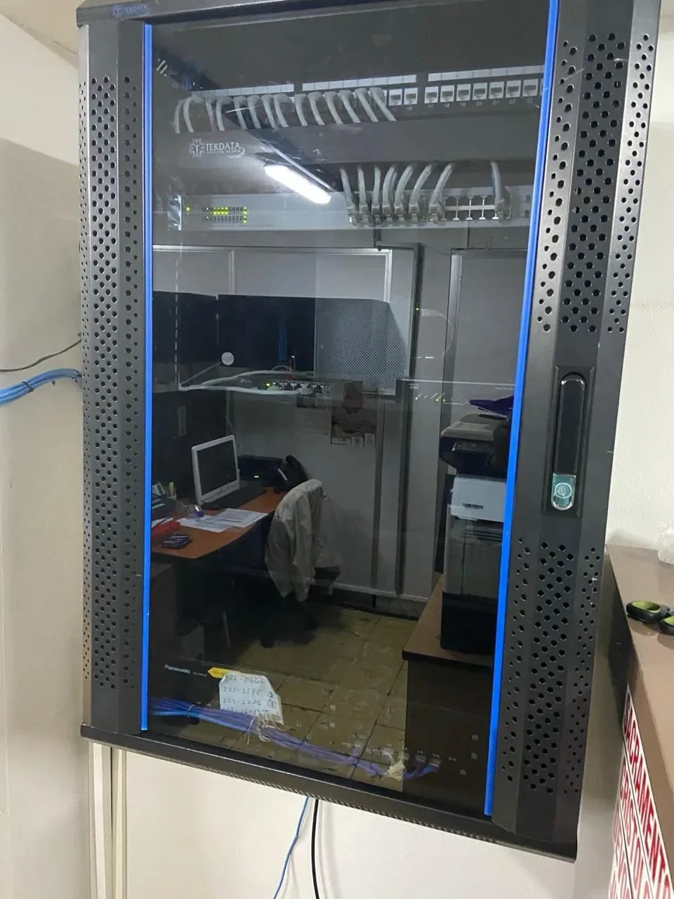 Gabinete de red con puerta de cristal que muestra cables y equipo de red en su interior.