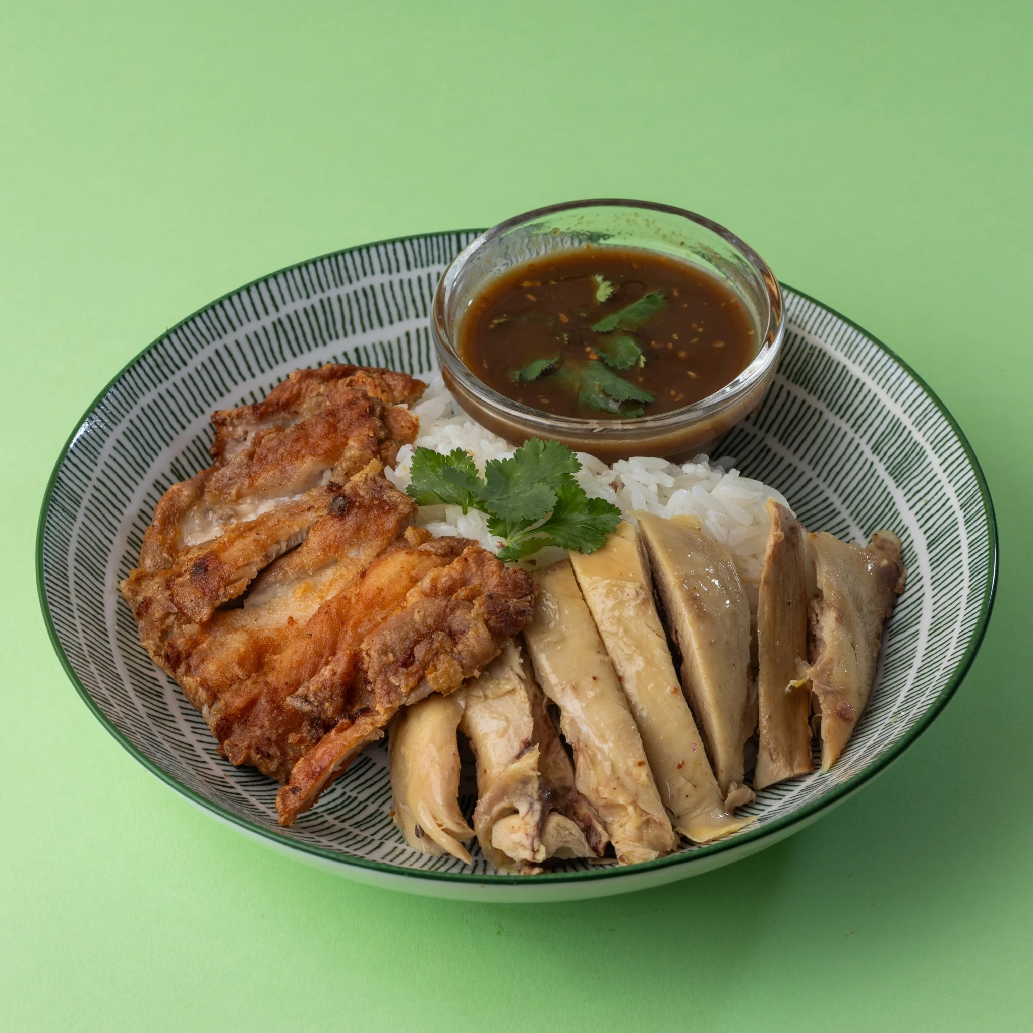 Plate of fried chicken with rice, sliced chicken, and a bowl of brown dipping sauce garnished with cilantro on a green background.