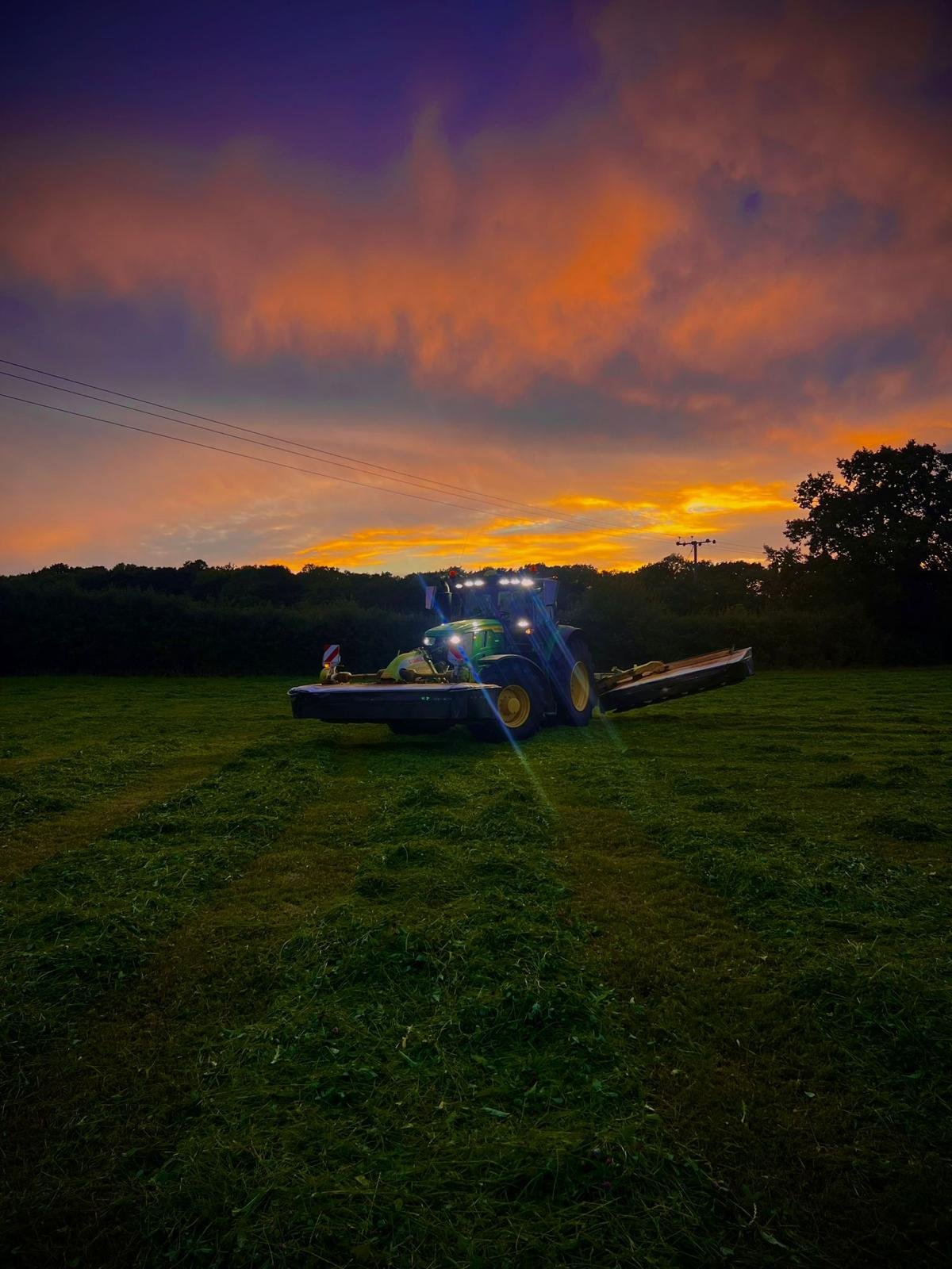 A large tractor working on a field during sunset with a colorful sky.