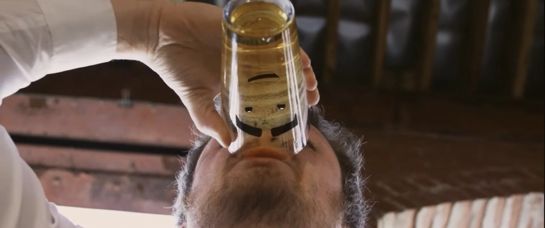 Person holding a glass with a smiley face design, drinking from it, viewed from below.