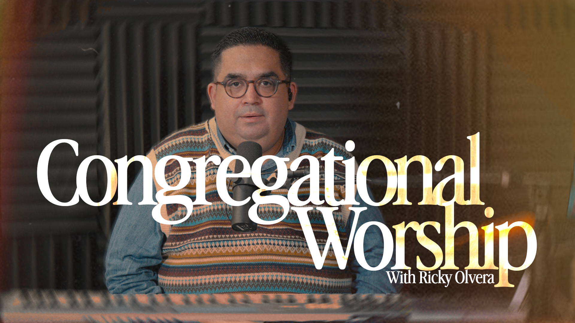 A man with dark hair, glasses, and wearing a patterned sweater, sitting at a piano with a microphone in front of him, with the text "Congregational Worship with Ricky Olvera" overlaid.