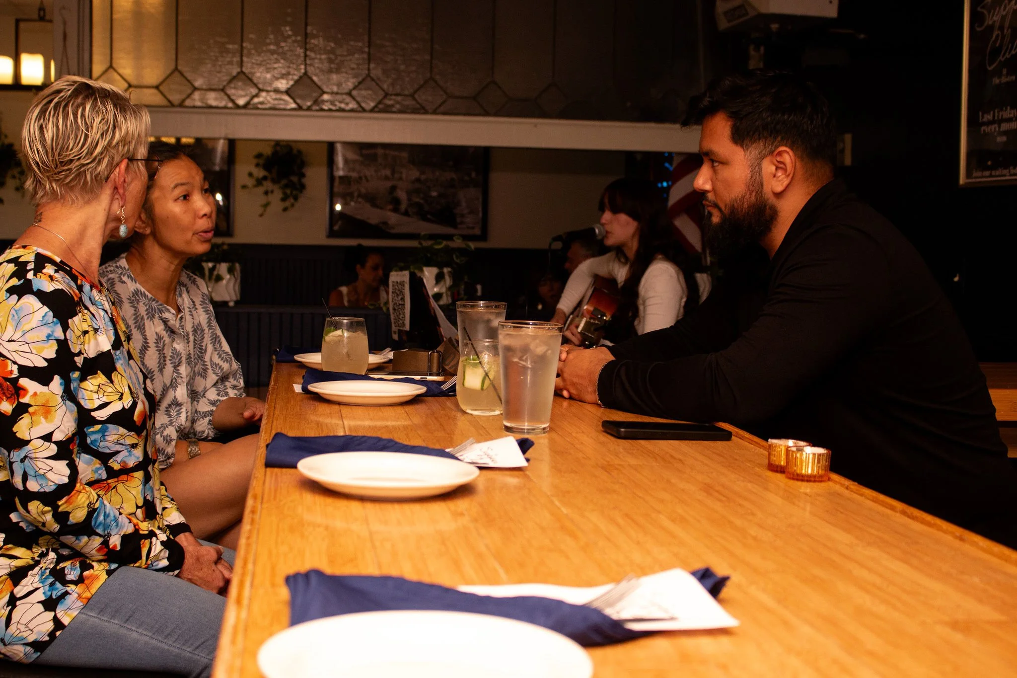 Group of people sitting at a bar, engaged in conversation, with drinks on the counter.