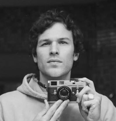 Jesy McKinney is on staff at Carmel Church in San Diego. He helps in creative arts, Youtube, videos, social media, etc and builds the christian community. Black and white photo of a young man taking a selfie with a vintage camera, wearing a hoodie.