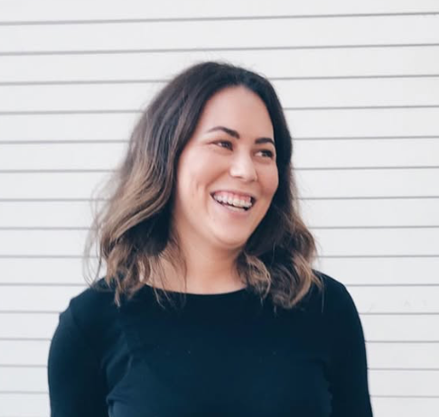 Jen McFadden is on staff at Carmel Church in San Diego. She helps in finances and builds the Young Adults singles. A young woman with shoulder-length brown wavy hair smiling and looking to the side, standing in front of a white horizontal-lined wall.