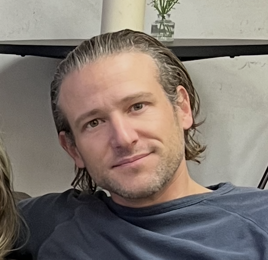 Jery McKinney is on staff at Carmel Church in San Diego. He helps in creative arts, Youtube, videos, social media, etc and builds the christian community. A man with long brown hair, wearing a dark shirt, sitting indoors with a neutral expression.