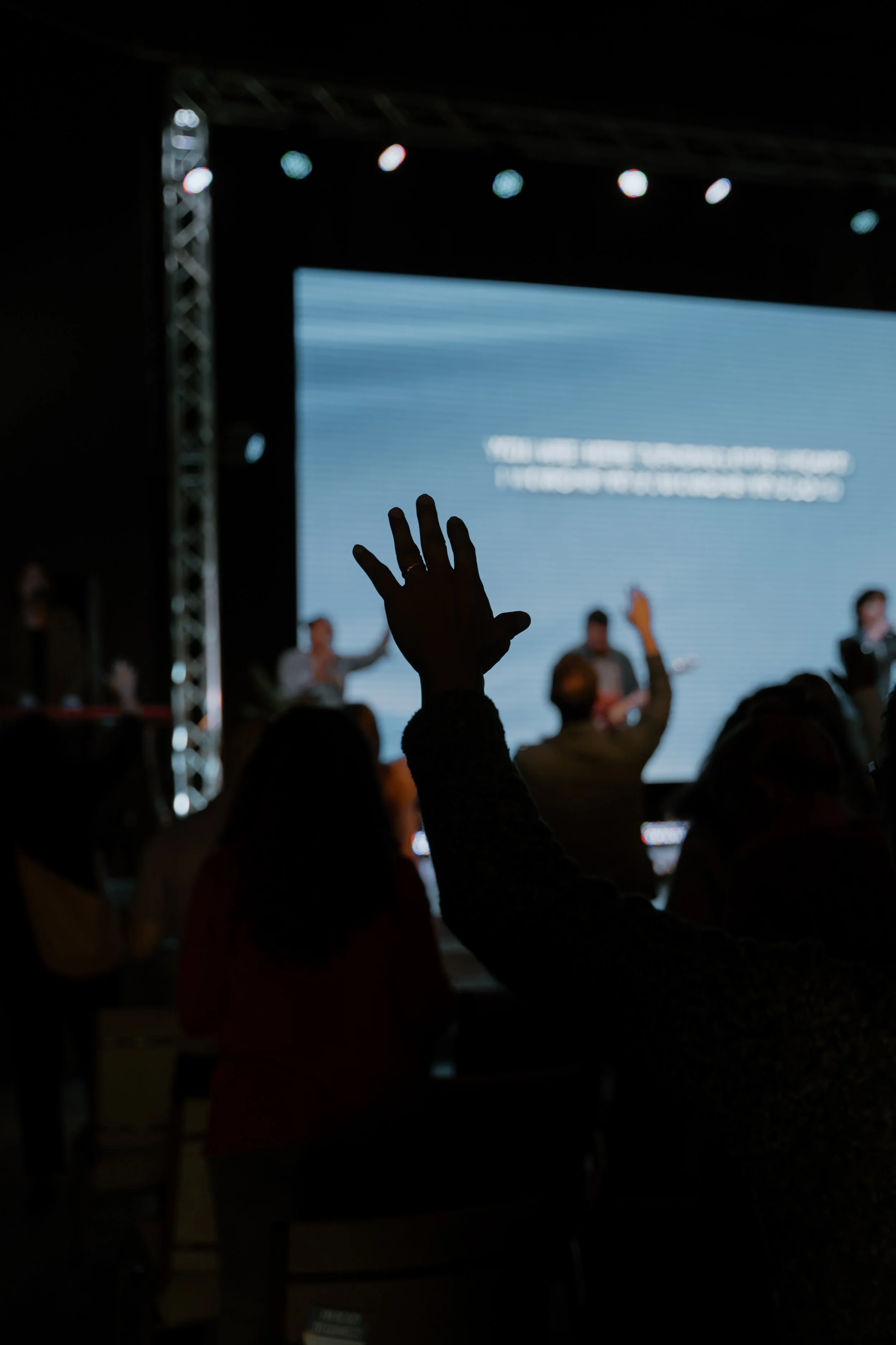 Audience raising hand during a presentation or performance on stage in a dark auditorium.