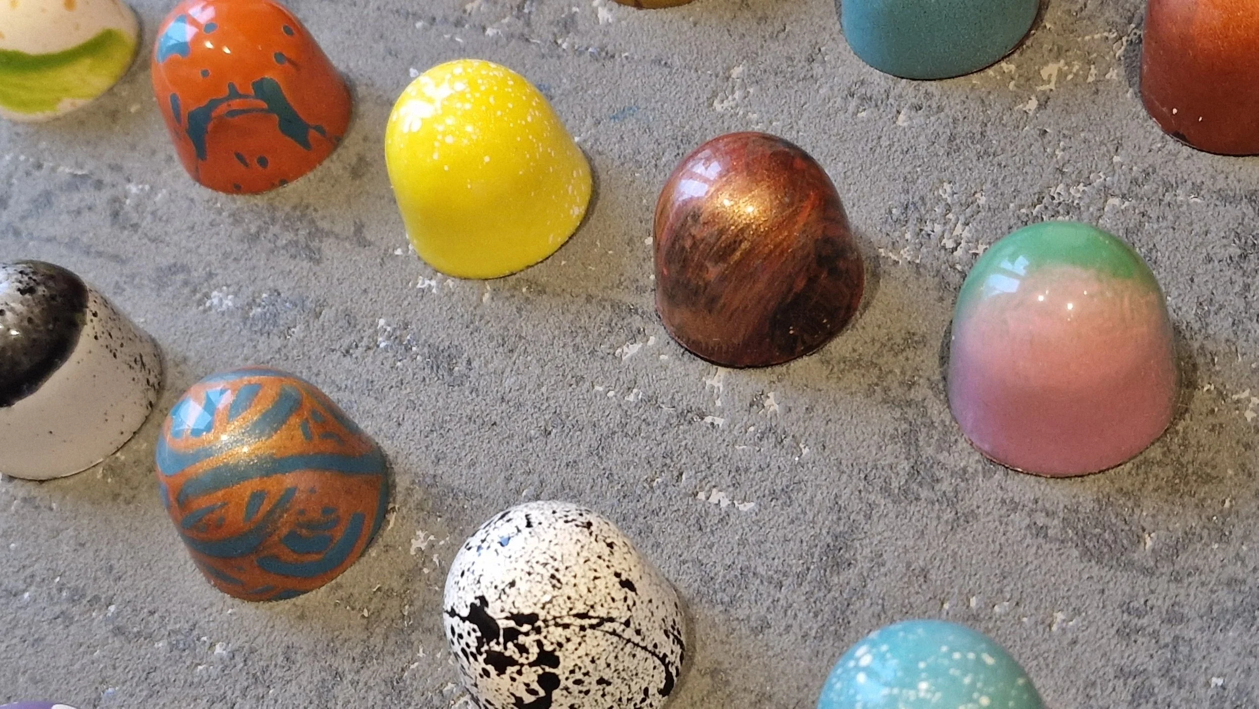 Colorful painted rocks on a sandy surface, arranged randomly with various colors and patterns.