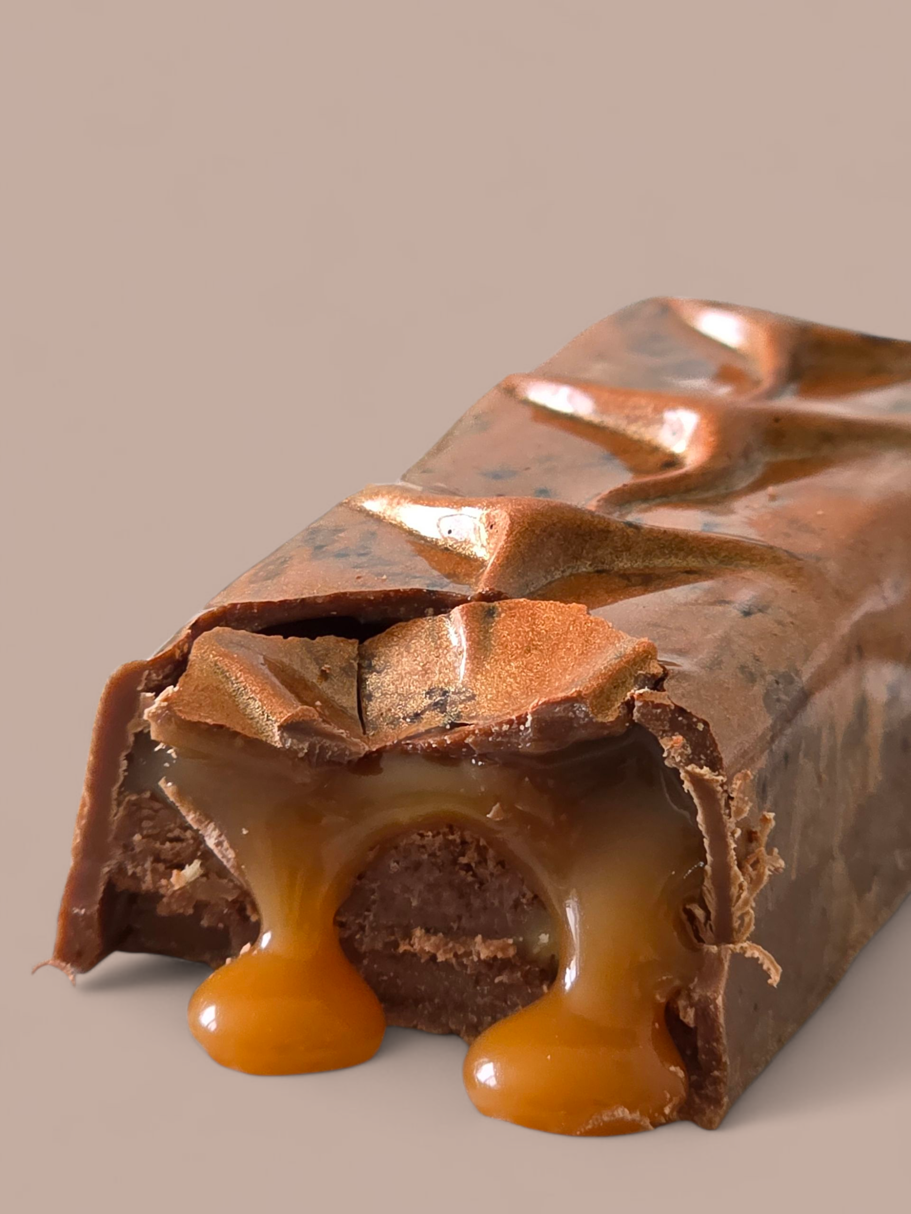 Close-up of a partially eaten caramel-filled chocolate candy bar with gooey caramel oozing out, set against a neutral background.