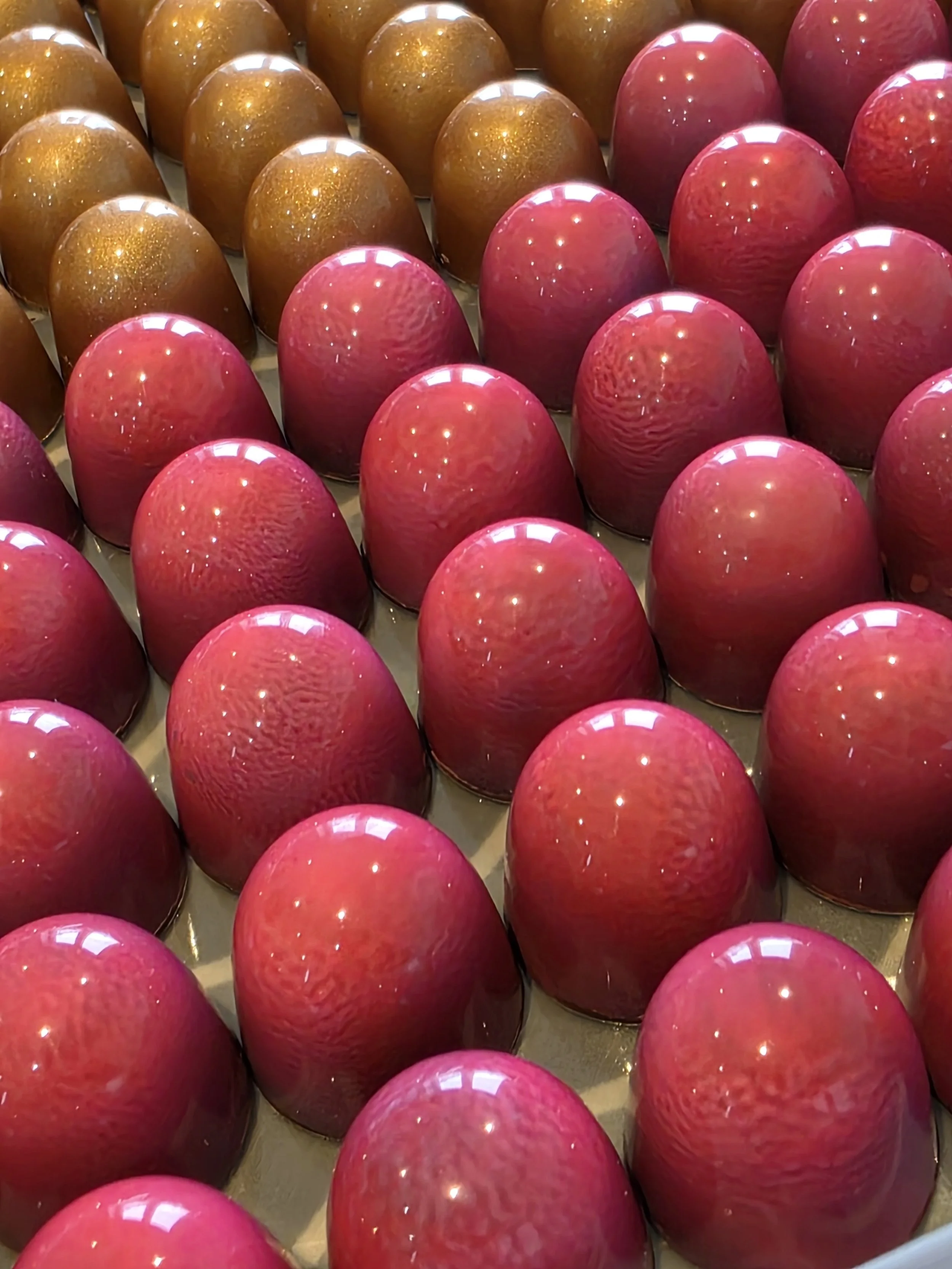 Rows of pink and brown chocolates with shiny, smooth surfaces arranged on a tray.