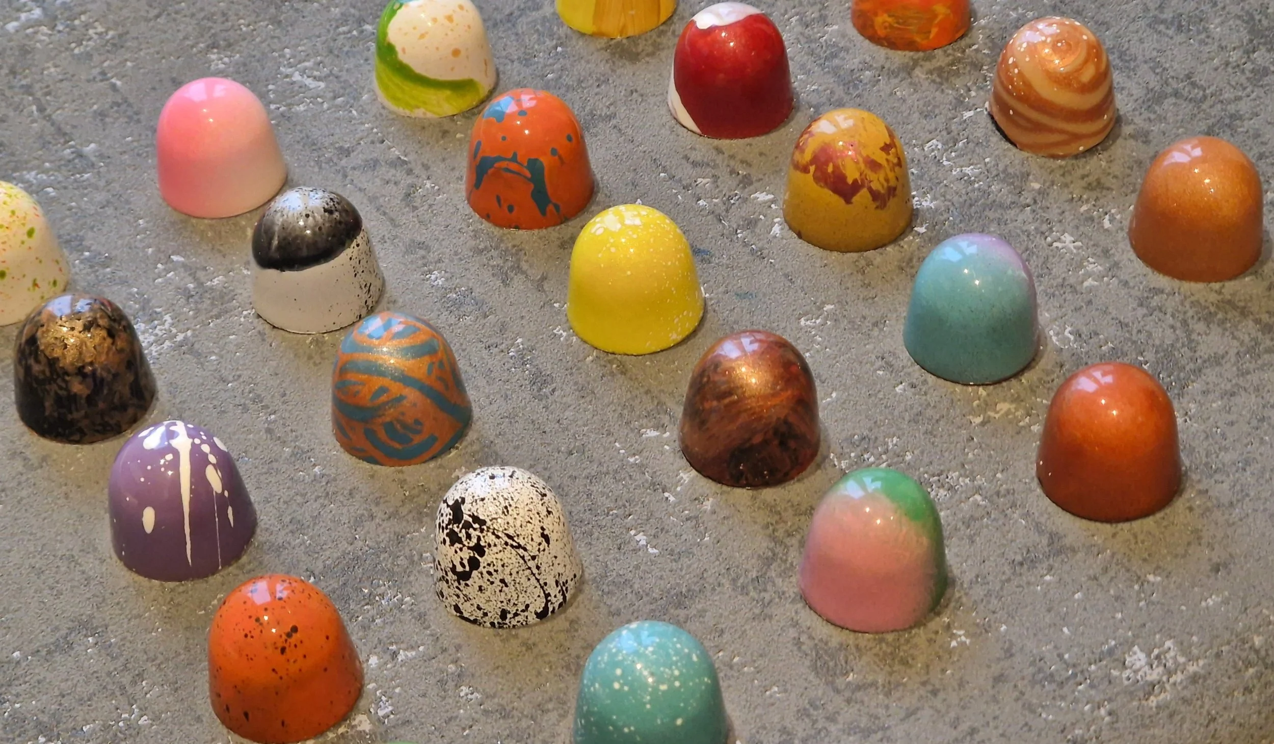 Colorful marbled and speckled chocolate candies arranged on a gray surface.