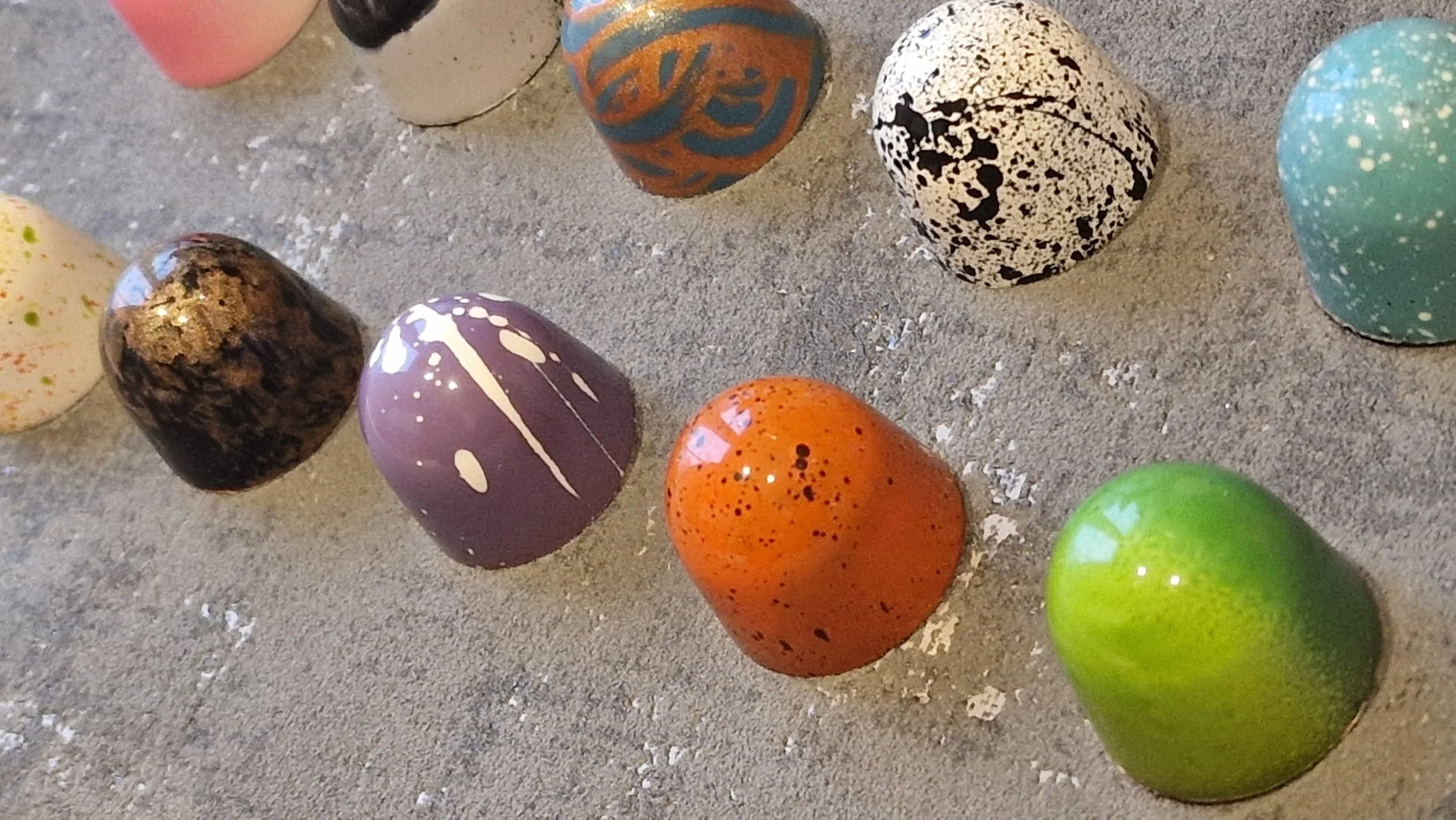 Colorful, painted chocolate bonbons placed on a sandy surface.
