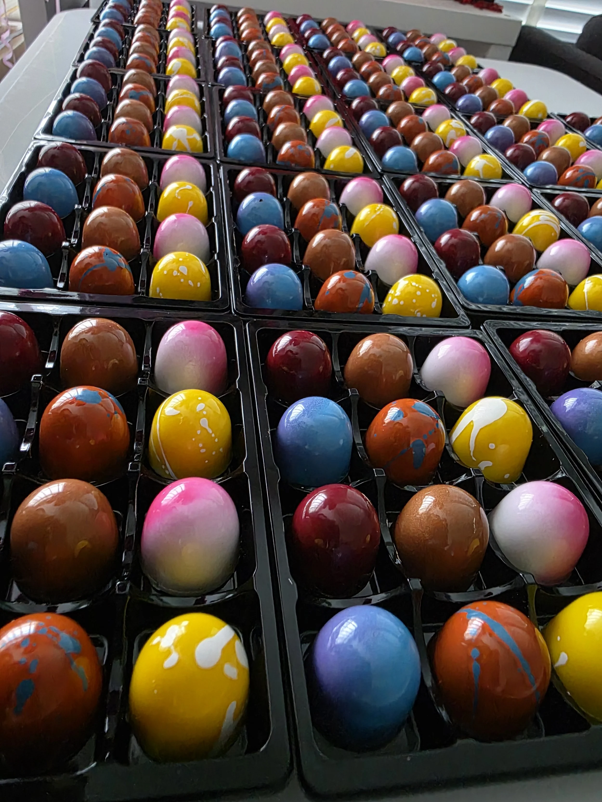 Colorful painted bonbons arranged in black tray.