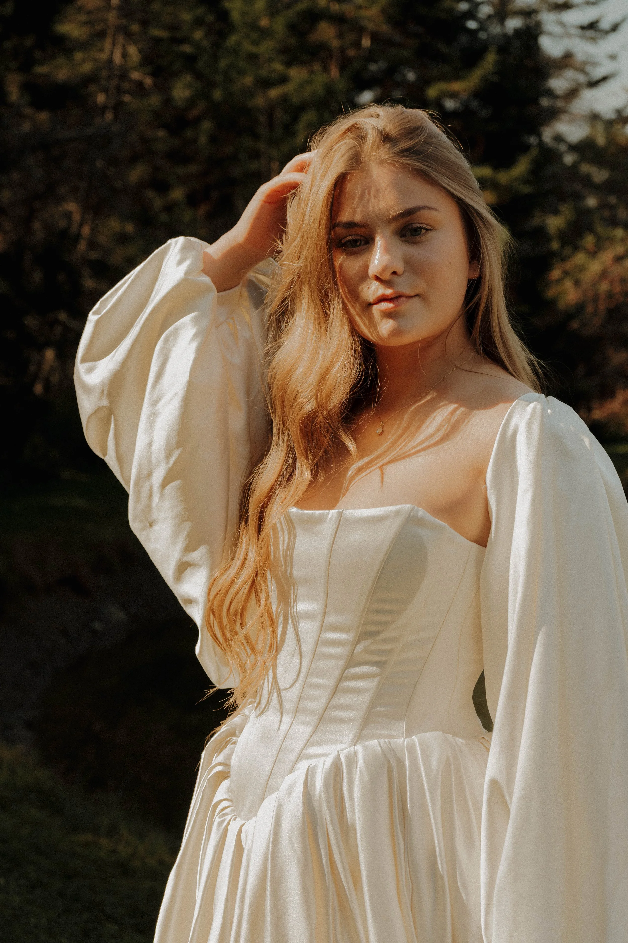 Irasburg, Vermont Young woman in a cream-colored dress outdoors, sunlight on her hair and face, with trees in the background.