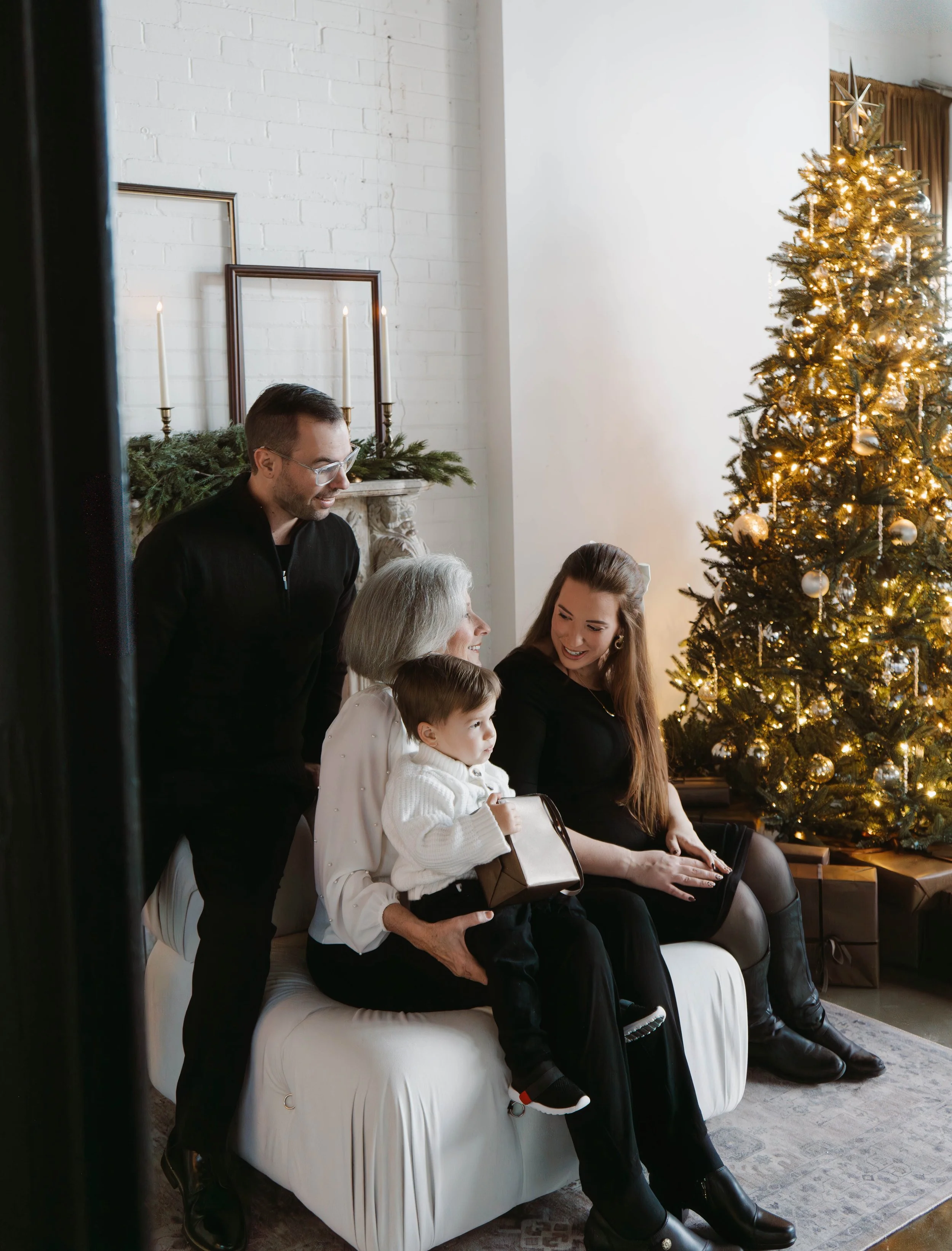 Pose Studio Photographer, A family gathered around a Christmas tree with presents, sitting on a white couch in a decorated living room.