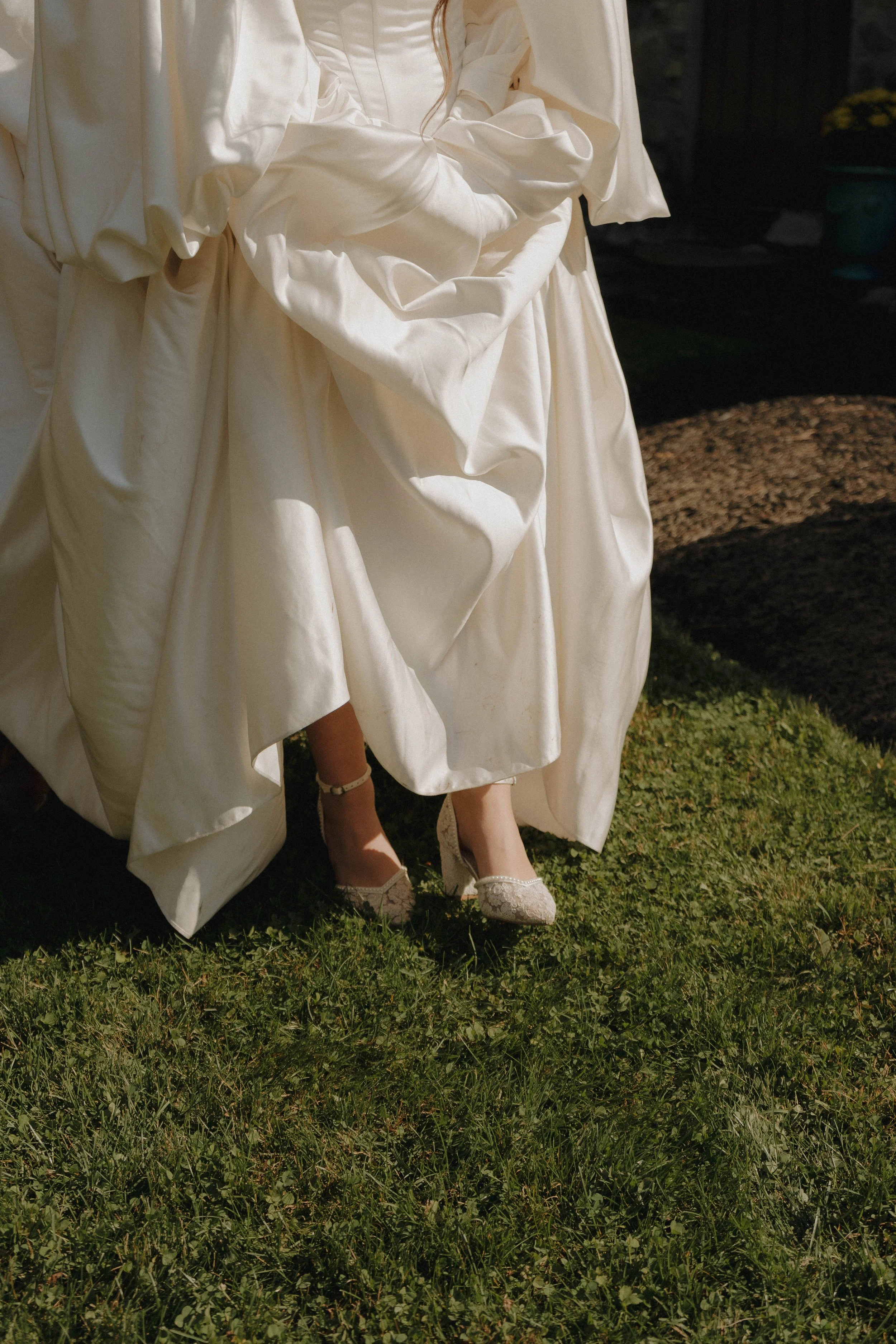 Close-up of a bride's dress with sparkly heels as she stands on green grass in sunlight.