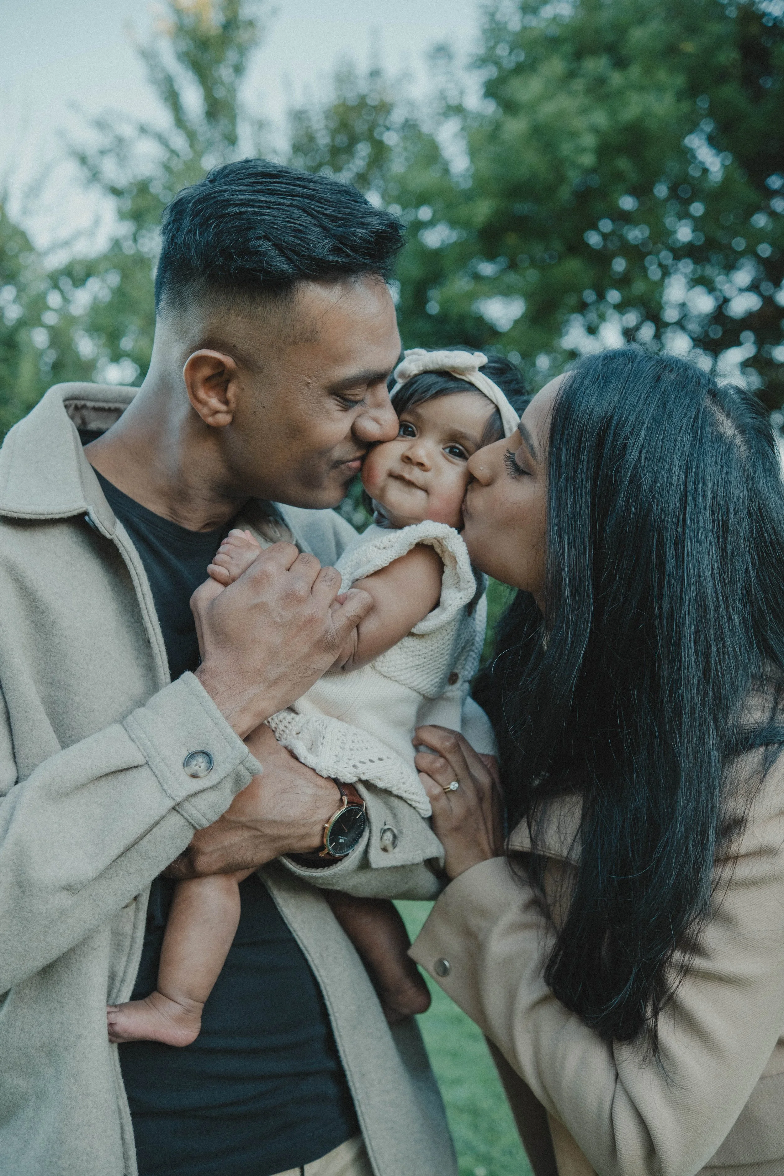 Burnet Park, Syracuse NY A family outdoors, a man and woman kissing their baby girl on the cheeks.